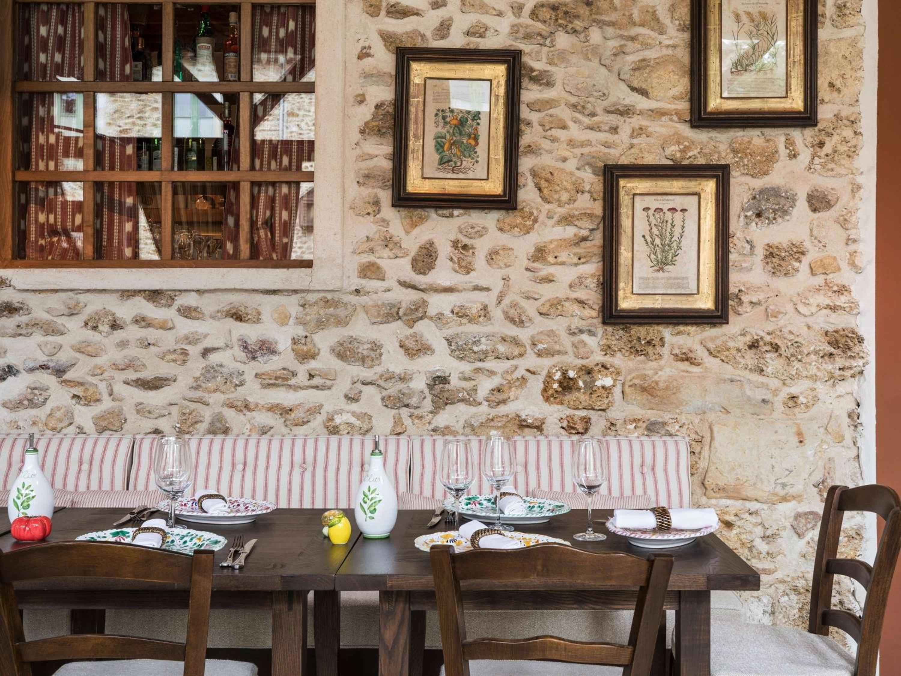 Stone walls and botanical prints create intimate dining nooks where striped banquettes frame rustic wooden tables set with artisanal ceramics and flickering candlelight.