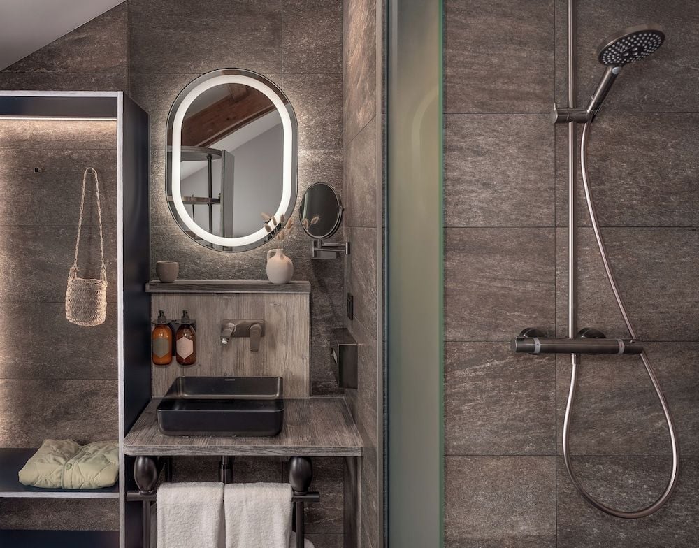 Charcoal stone tiles and weathered wood create an intimate sanctuary where industrial fixtures meet organic textures in perfect minimalist harmony.