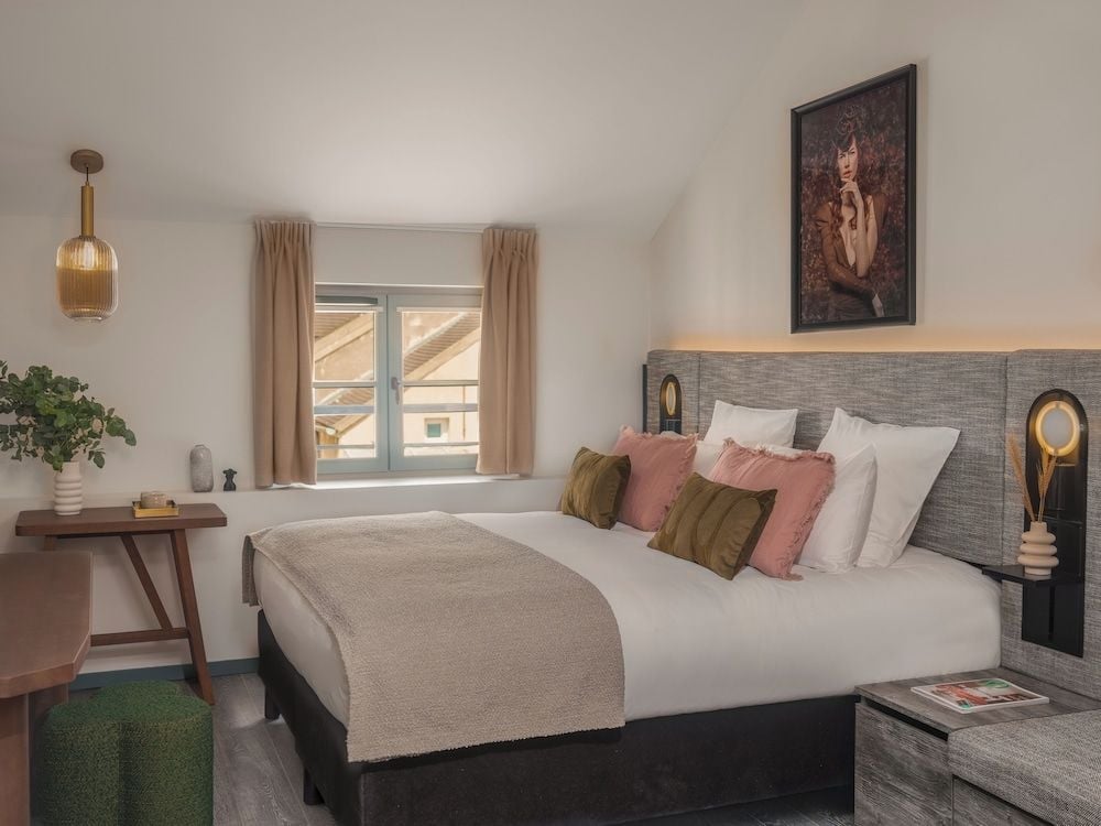 Soft natural light filters through gauze curtains, illuminating coral and olive pillows against textured headboards in this intimate sanctuary where modern comfort meets artistic flair.