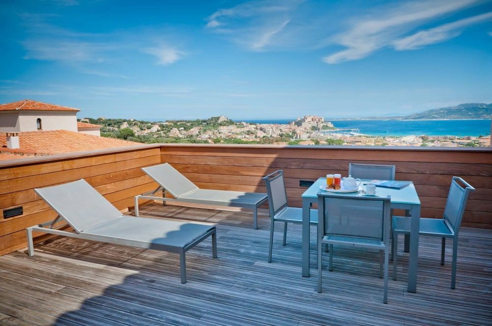 Modern loungers and sleek dining furniture frame panoramic views of Calvi's terracotta rooftops cascading toward the sapphire Mediterranean from this sophisticated rooftop terrace.