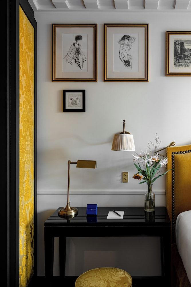 Golden damask wallpaper frames an intimate writing nook where brass task lighting illuminates framed sketches, creating a literary salon atmosphere in this thoughtfully curated Parisian retreat.