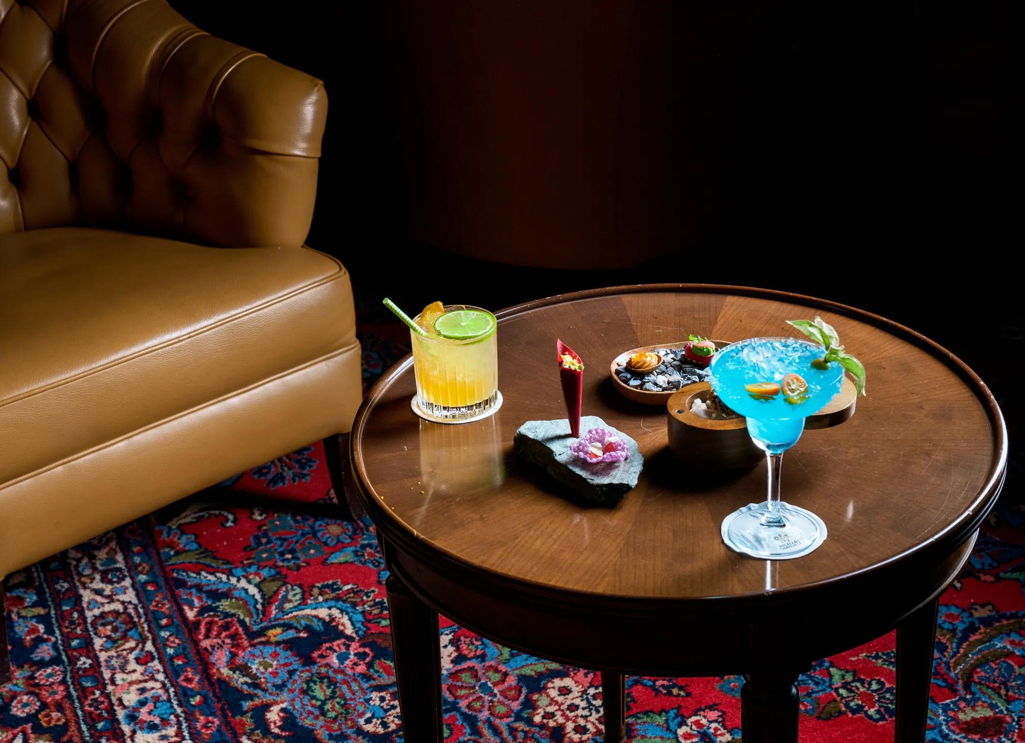 Artfully crafted cocktails and elegant canapés await on polished wood tables, where leather banquettes and Persian rugs create an intimate lounge atmosphere.