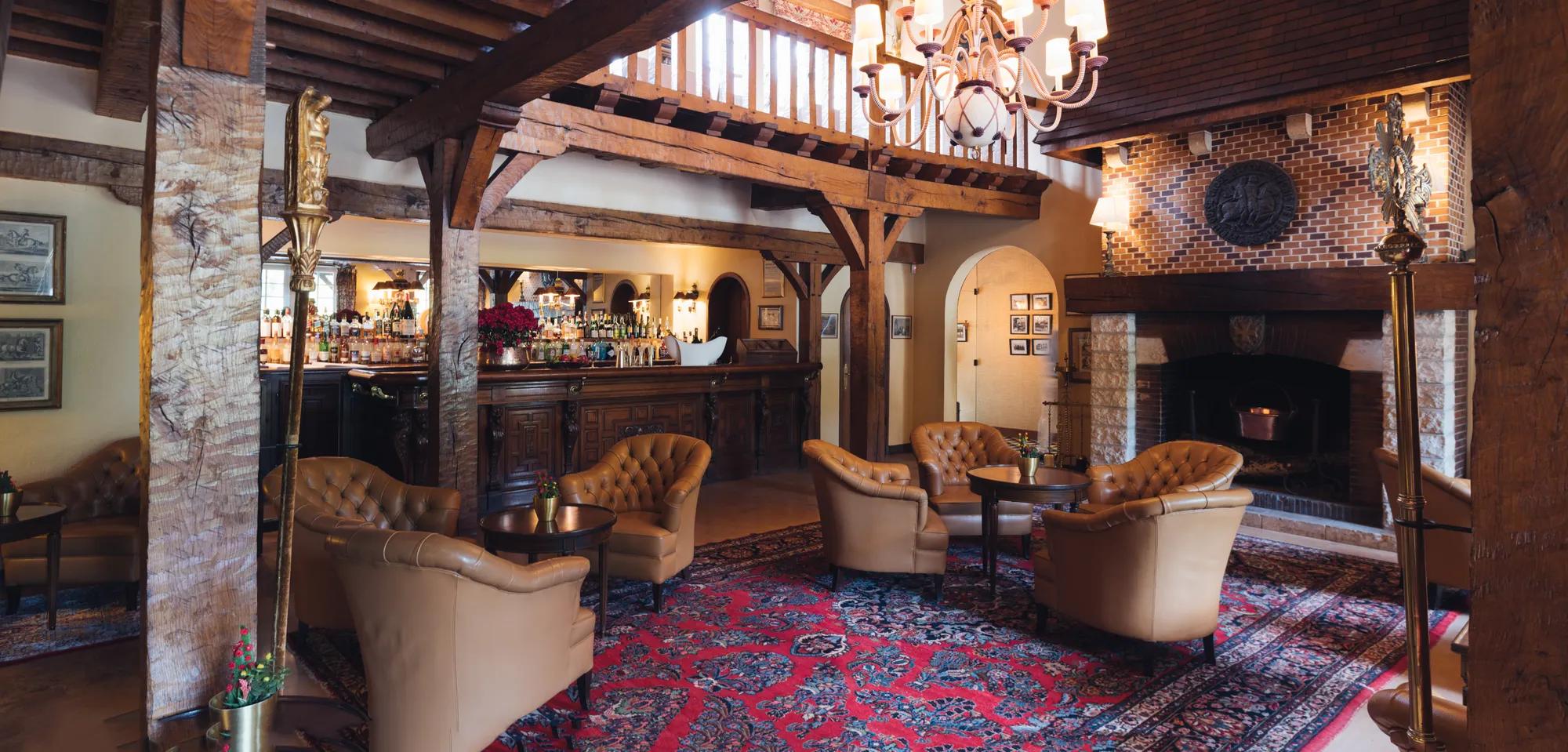 Exposed timber beams and tufted leather armchairs create an intimate lounge where Persian rugs warm flagstone floors beside a crackling brick fireplace.
