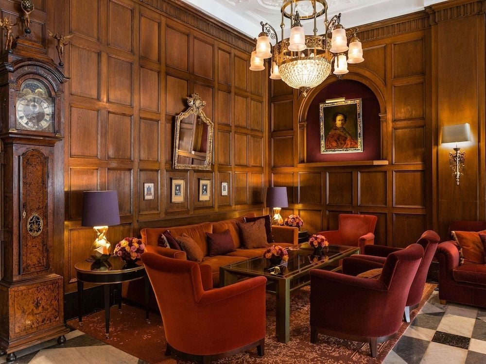 Rich walnut paneling and burgundy velvet armchairs create an intimate reading salon, where crystal chandeliers cast golden light across oil portraits and an ornate grandfather clock.