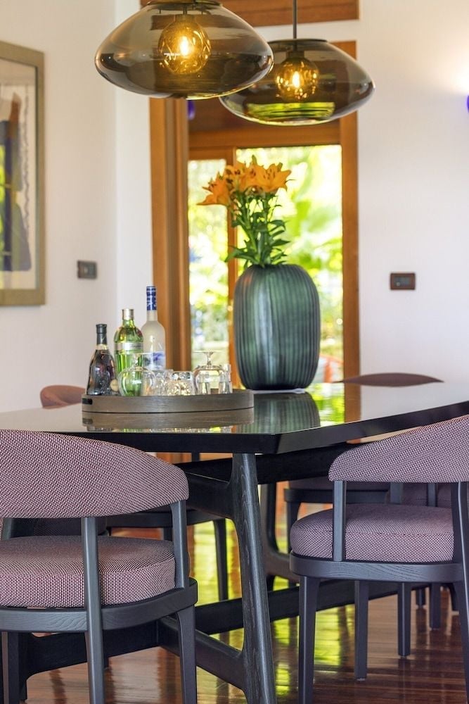 Modern pendant lights cast a warm glow over the sleek dining area, where orange blooms in a ceramic vase complement the rich wood frames and contemporary furnishings.