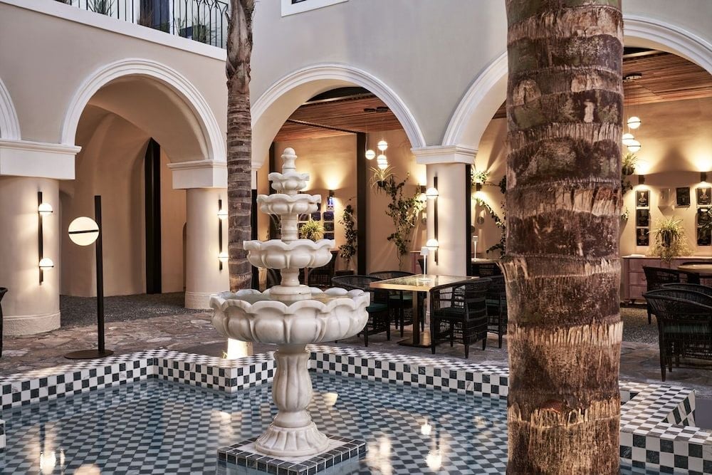 Moorish arches frame an elegant courtyard where checkered tiles meet whitewashed columns, creating intimate seating nooks beneath warm ambient lighting and graceful palm fronds.