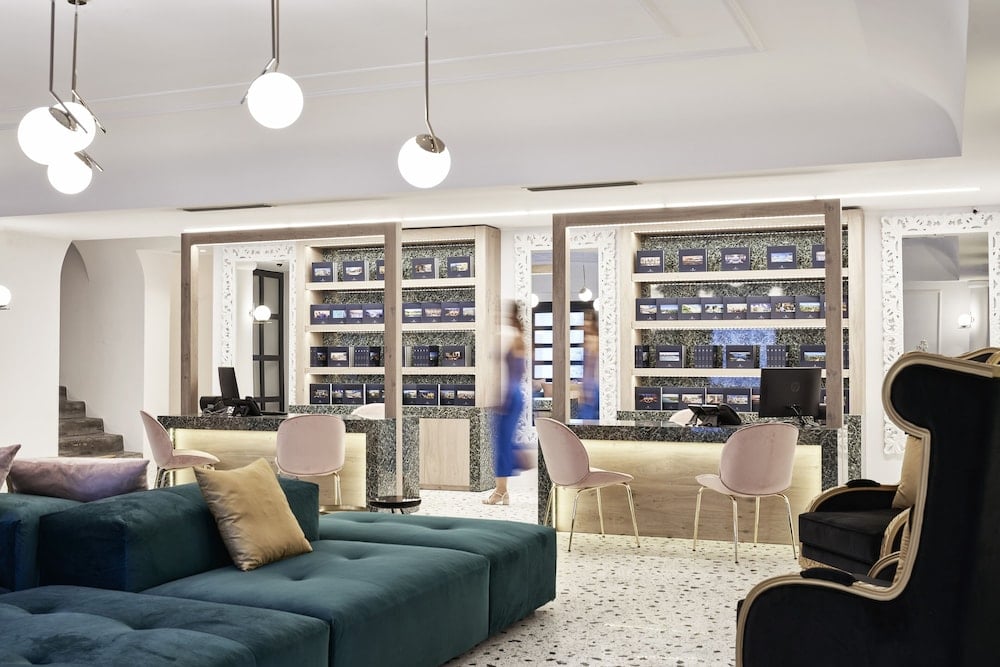 Spherical pendant lights cast a warm glow over the sophisticated lobby, where emerald velvet sofas invite lingering conversations beneath minimalist terrazzo floors and curated displays.