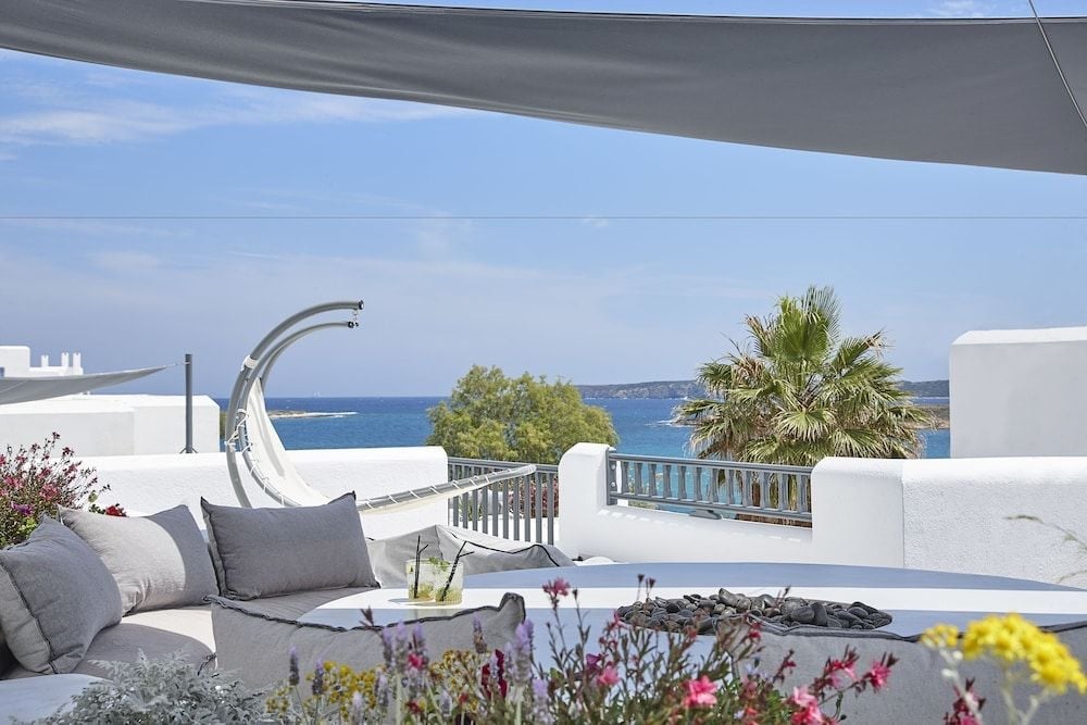 Sun-drenched terraces cascade toward azure waters, where white-washed walls frame the Aegean horizon and afternoon breezes carry the scent of Mediterranean blooms.