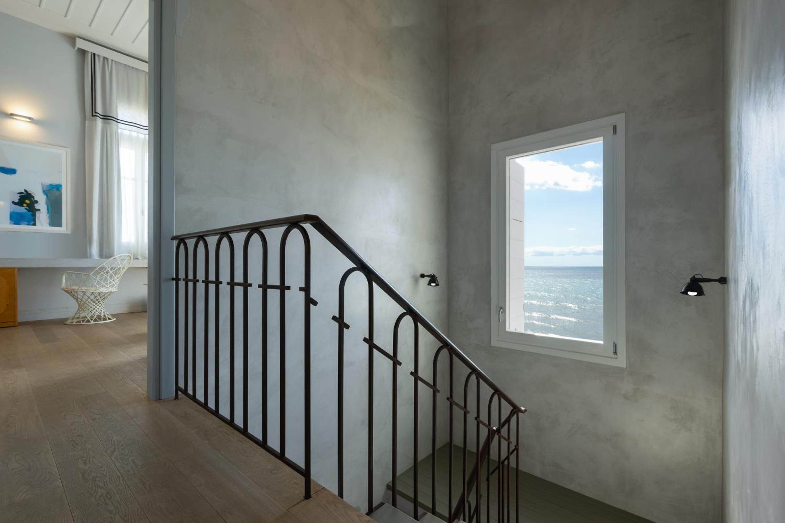 Polished concrete walls and wrought iron railings frame glimpses of the Ionian Sea through carefully positioned windows, where minimalist architecture meets coastal serenity.