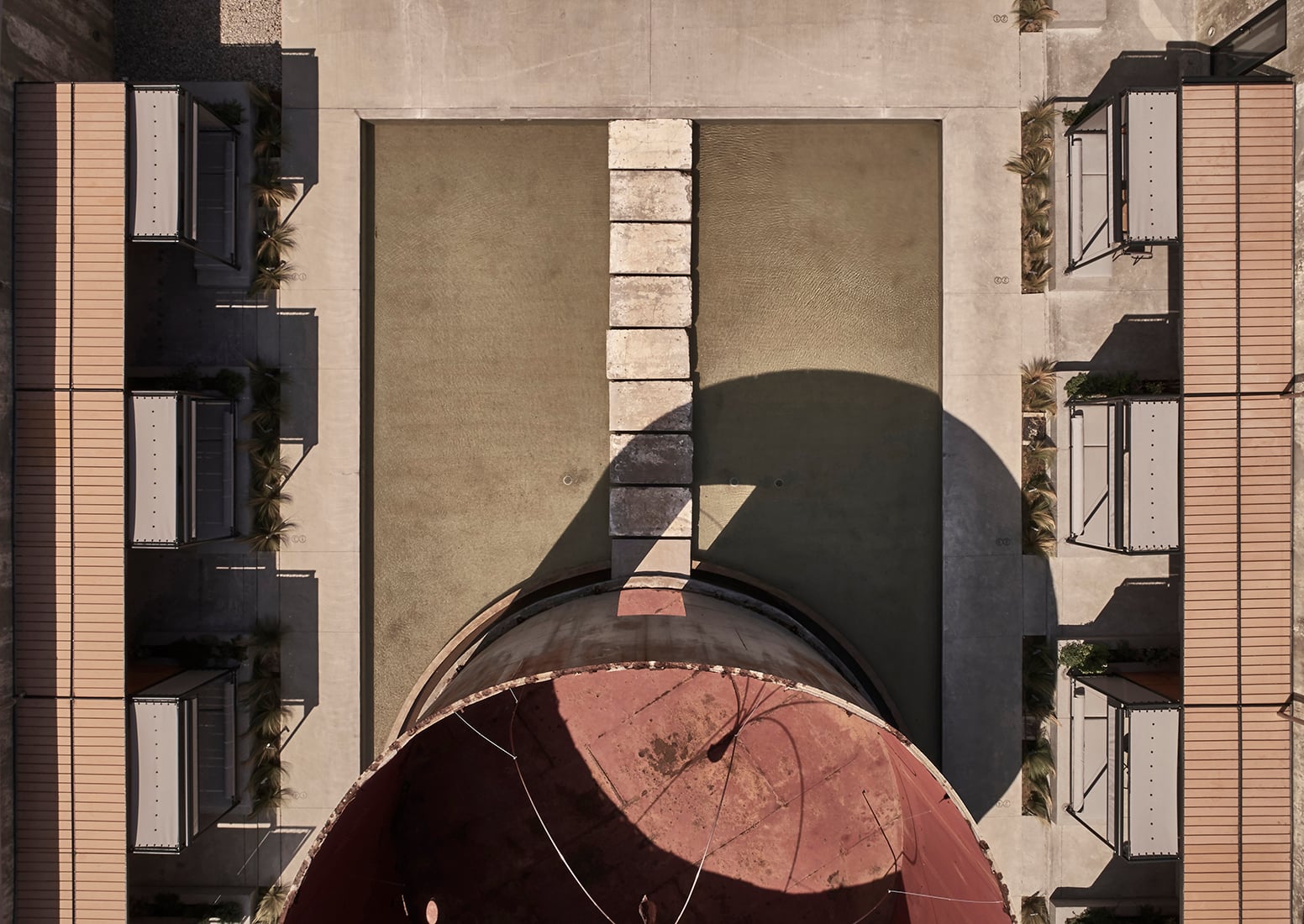 Concrete wine tanks reimagined as suites surround a dusty courtyard where shadows dance across terracotta tiles and weathered stone tells stories of industrial heritage transformed.