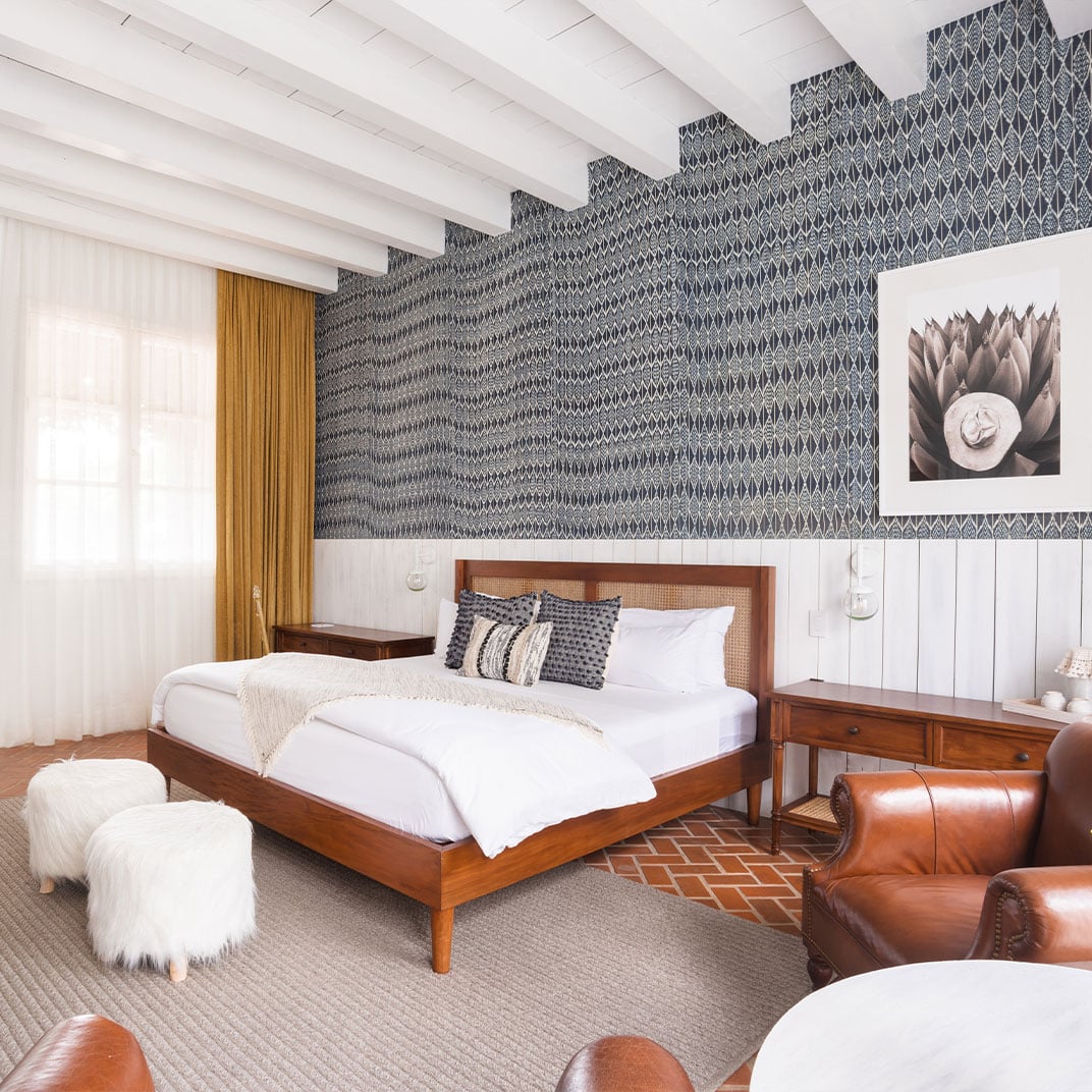 Geometric wallpaper cascades across exposed beams while warm walnut furniture and supple leather create an intimate sanctuary overlooking rolling vineyards.