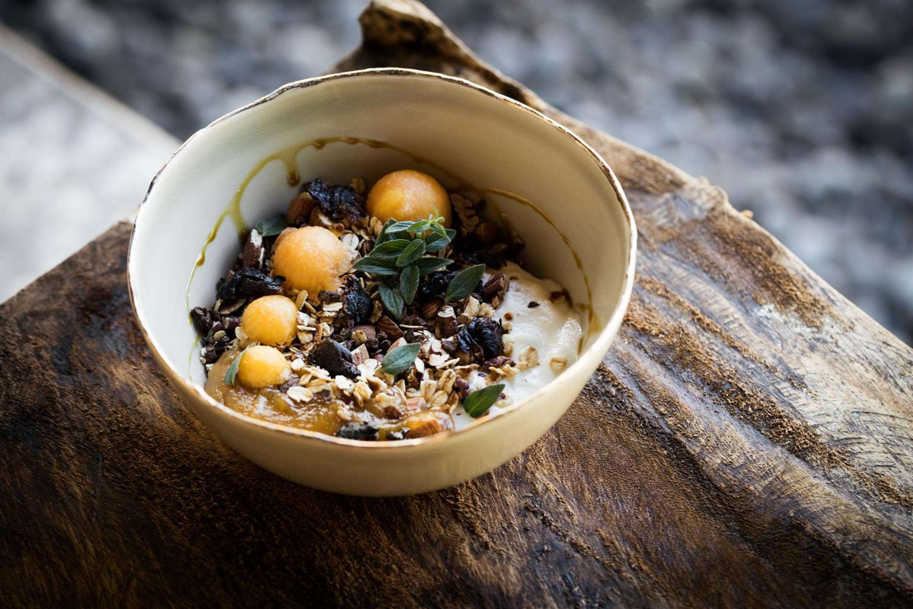 Artfully plated wellness cuisine arrives in handcrafted ceramic bowls, where golden chickpeas and dark grains create a nourishing mosaic against warm wood and natural textures.