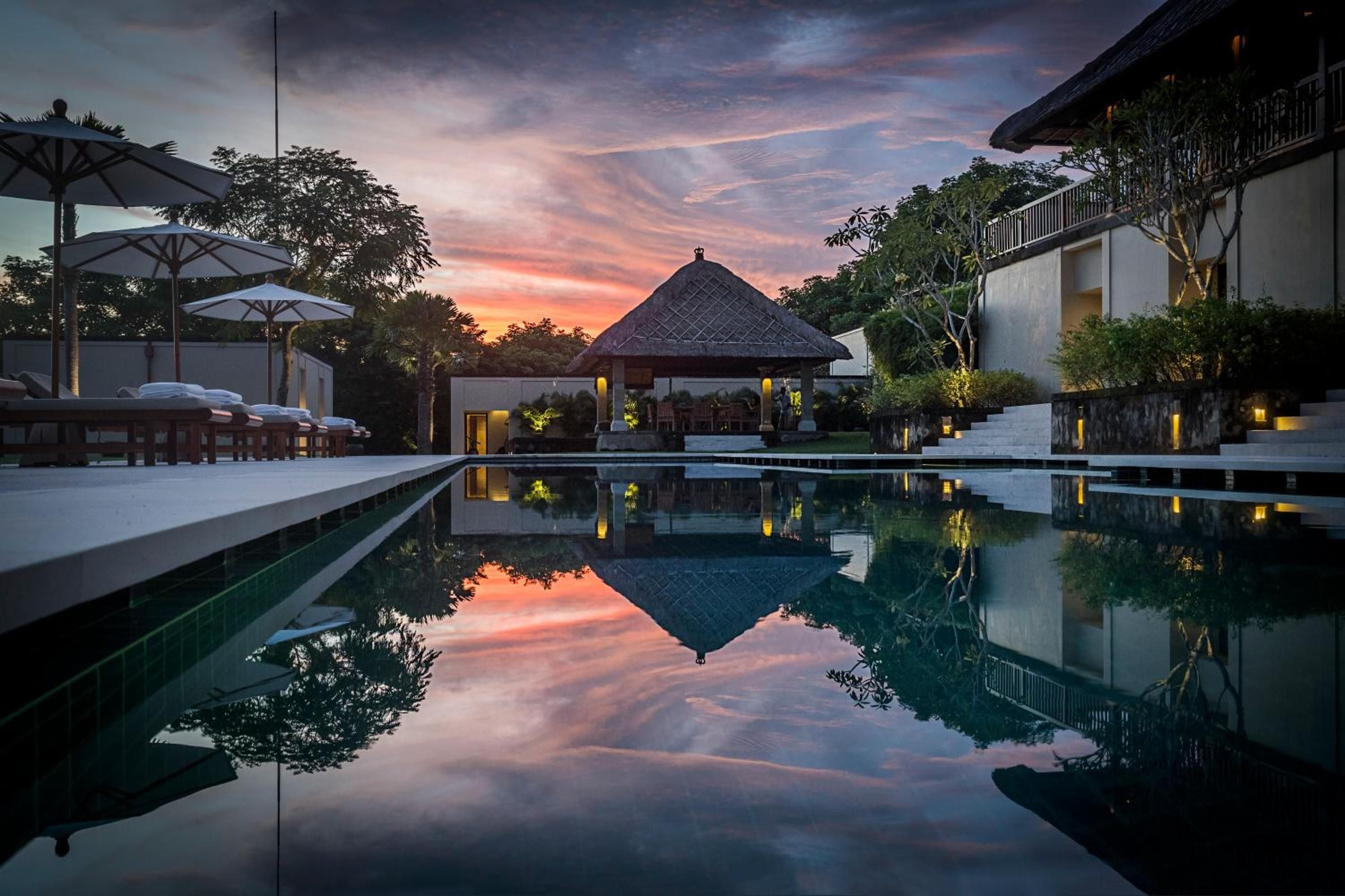 Dusk paints the sky in coral hues as traditional thatched pavilions reflect perfectly in the infinity pool's mirror-like surface, creating pure Balinese serenity.
