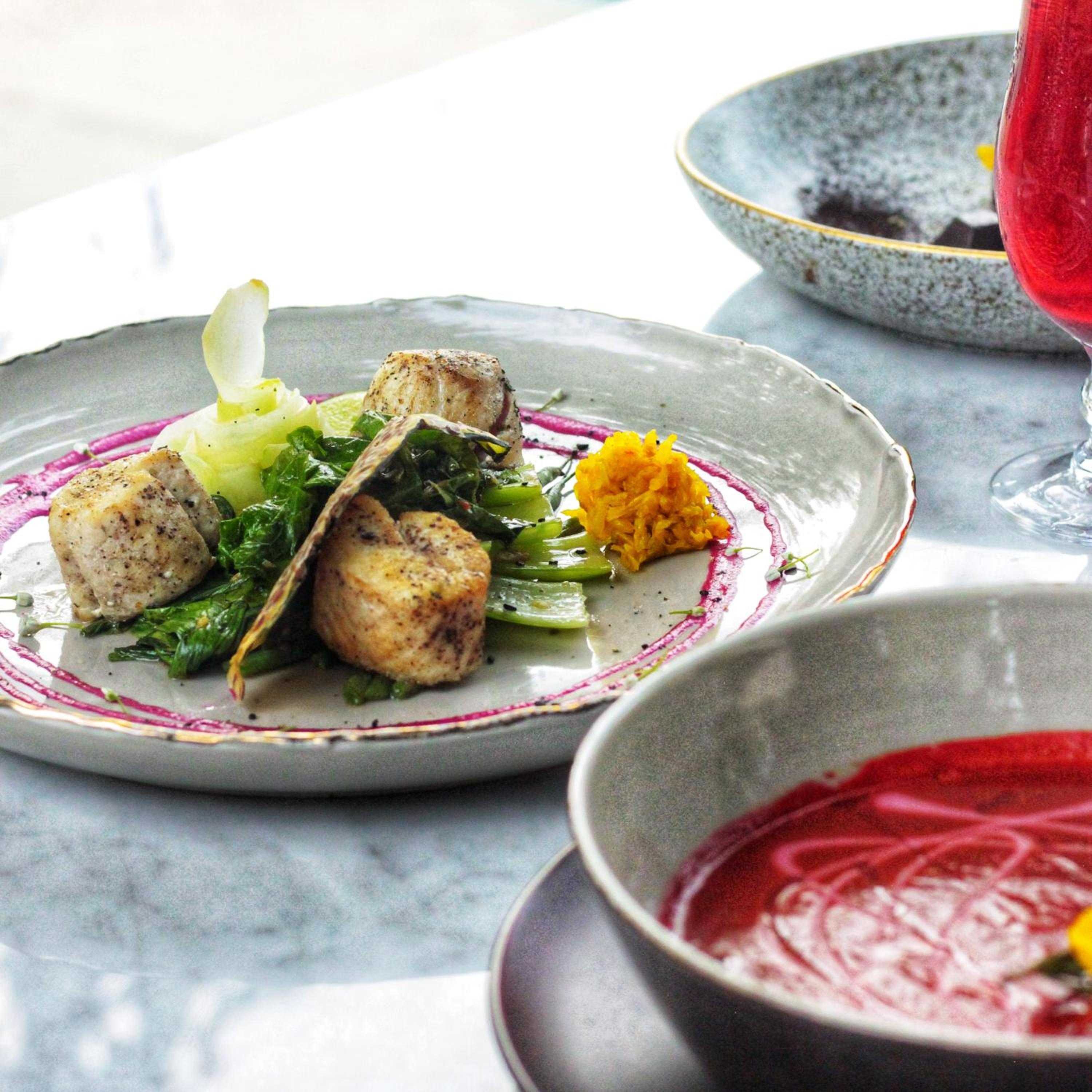 Artfully plated scallops arrive on handcrafted ceramics, their golden sears complemented by vibrant greens and delicate purple sauce swirls that mirror Bali's artistic heritage.