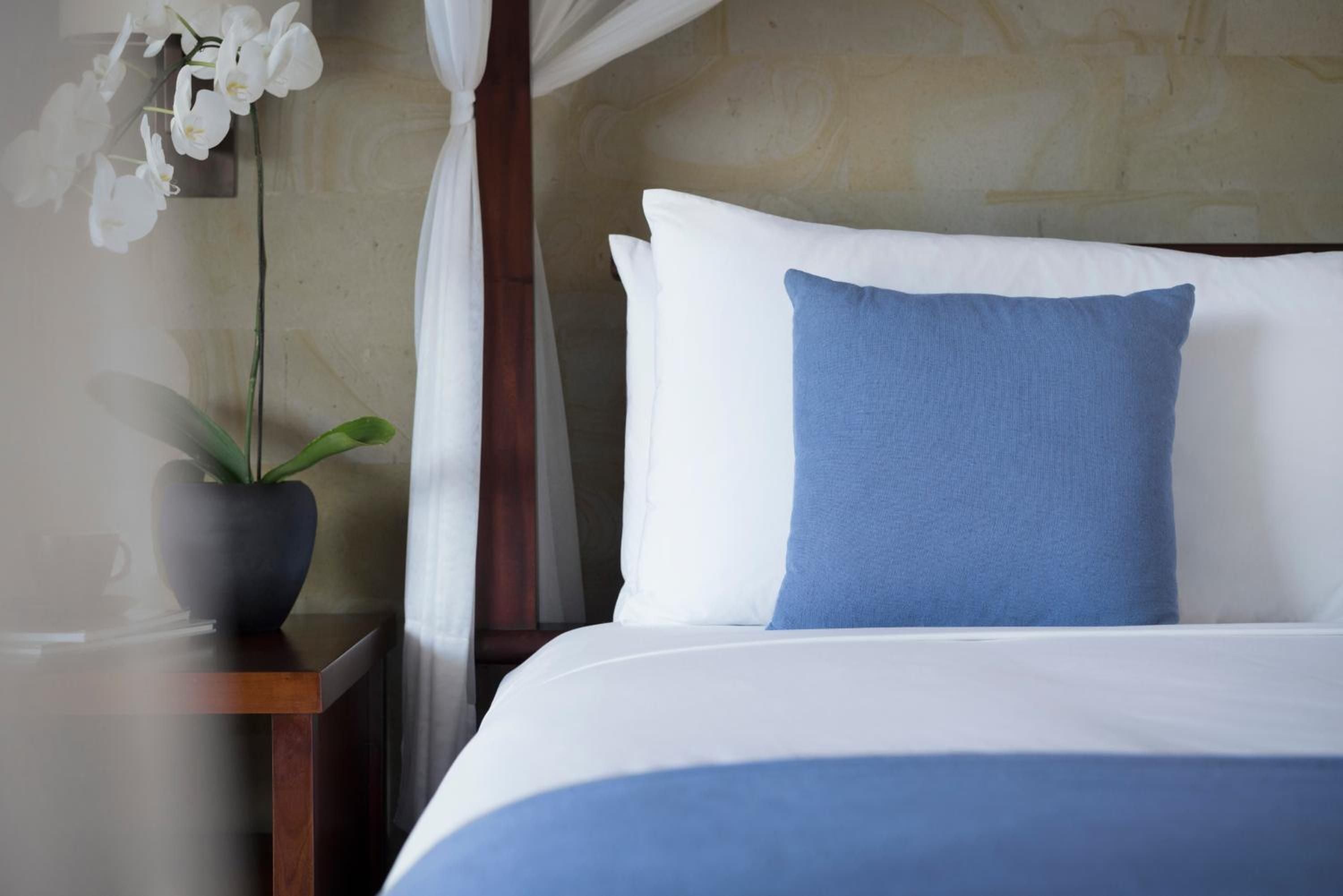 Crisp white linens meet ocean-blue accents in thoughtfully appointed accommodations, where fresh orchids and natural textures create a serene sanctuary for wellness-focused guests.