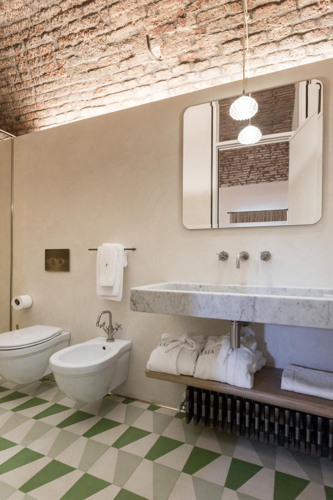 Exposed brick vaults frame a sculptural marble basin, while geometric floor tiles in sage and cream create playful contrast beneath pendant lighting.