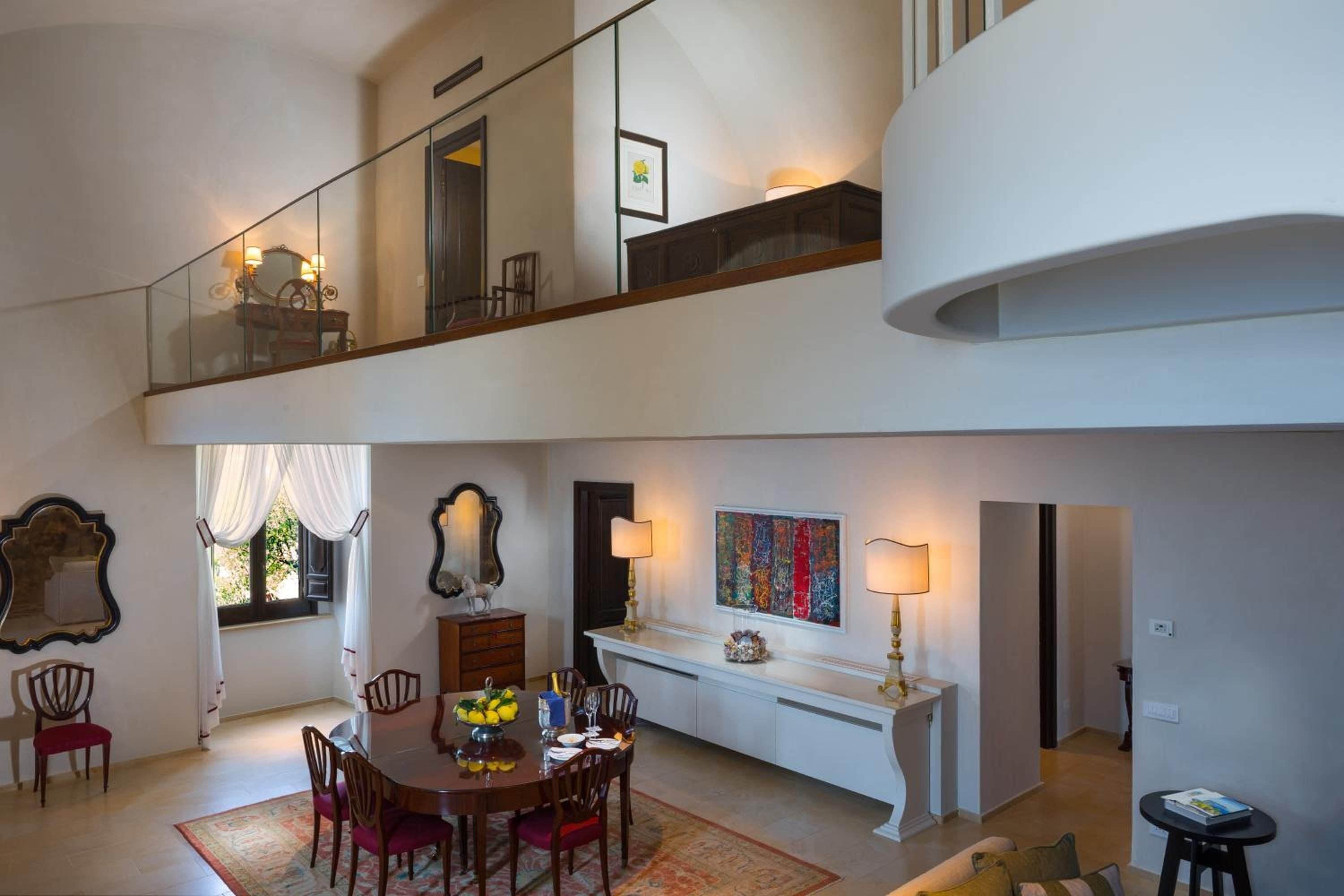 Soaring ceilings and glass railings frame this duplex suite where antique mirrors catch golden lamplight, blending monastic heritage with contemporary Italian elegance.
