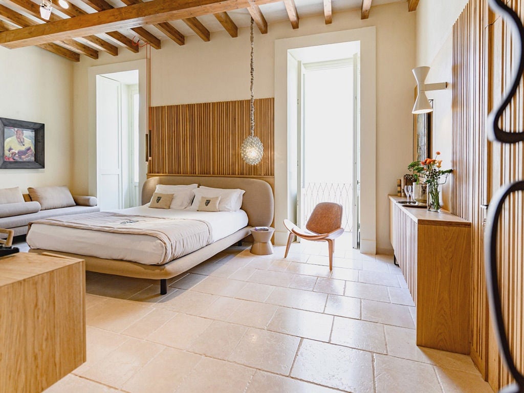 Exposed wooden beams frame this serene sanctuary where contemporary platform beds meet rustic stone floors, creating an intimate retreat bathed in Mediterranean warmth.