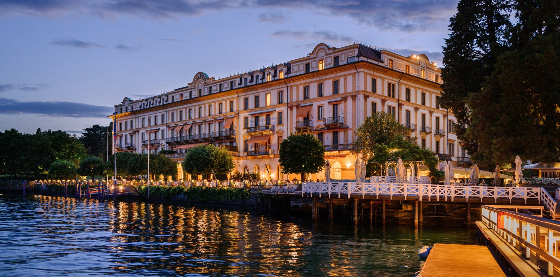 Golden hour illuminates Villa d'Este's Belle Époque facade as warm light dances across Lake Como's rippling waters and the hotel's iconic wooden pier.