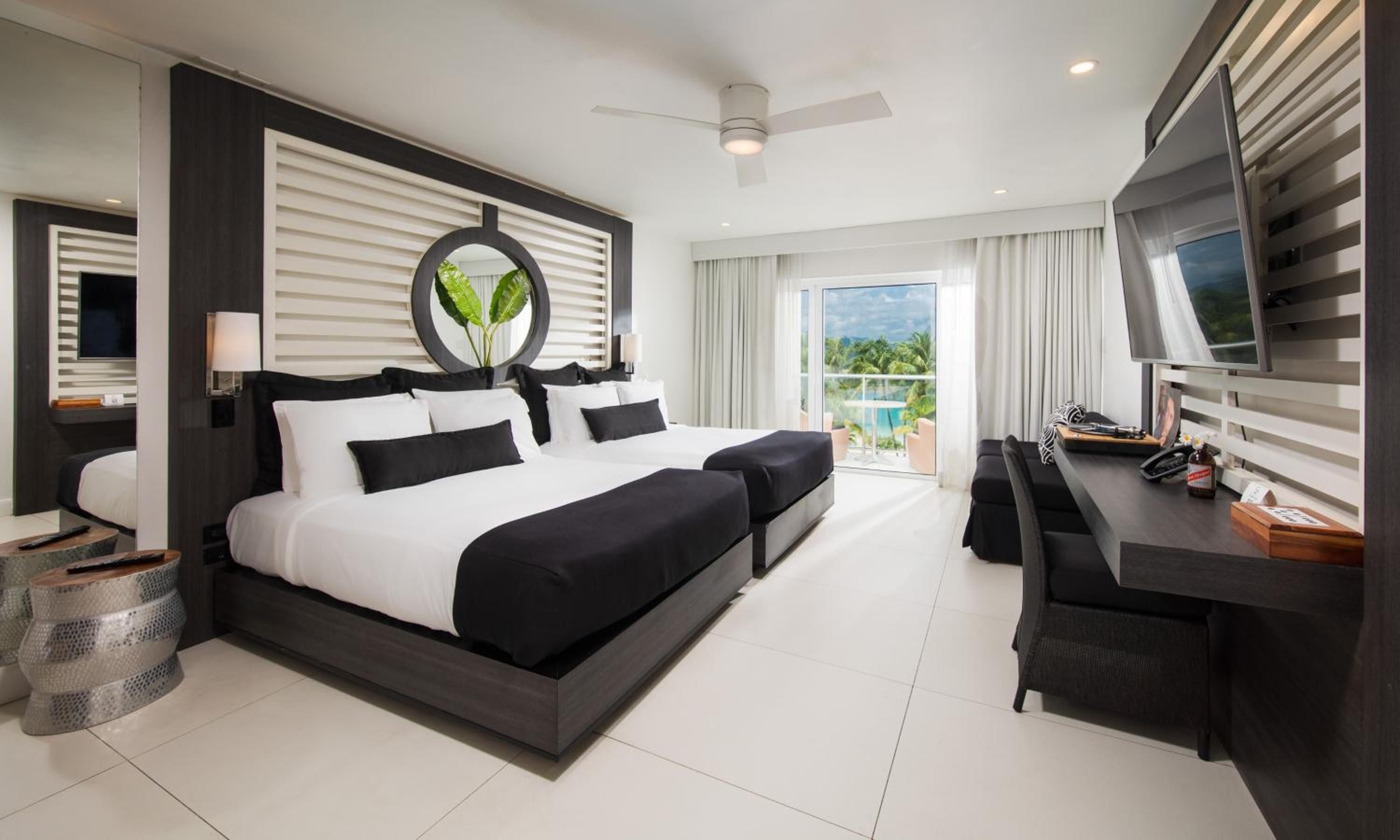 Contemporary elegance meets tropical sophistication in this sleek suite, where black lacquer furnishings and crisp white linens frame turquoise ocean glimpses beyond.