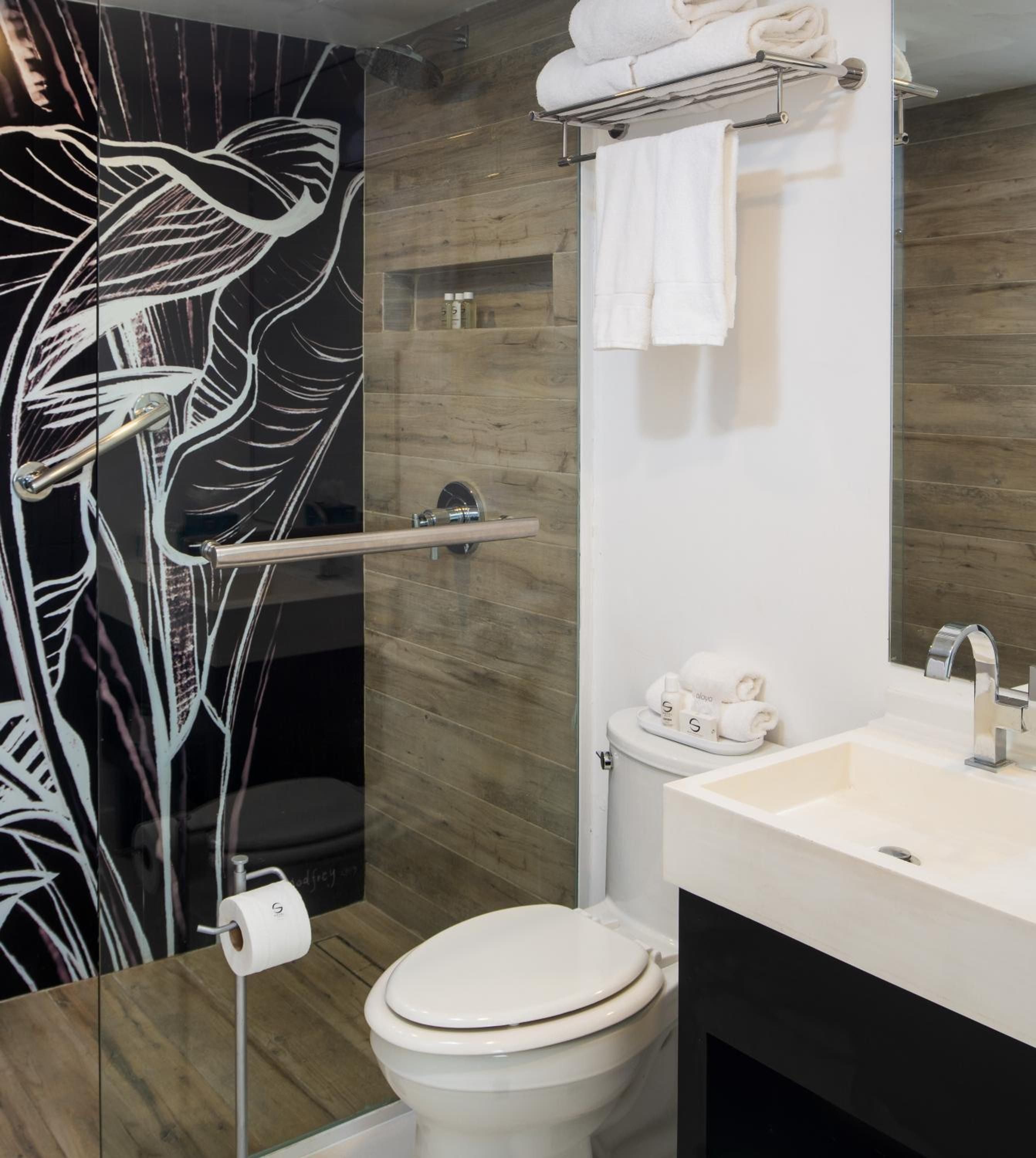 Bold tropical foliage artwork creates striking contrast against wood-grain tiles in this compact yet sophisticated bathroom, where white linens and sleek fixtures maximize the intimate space.