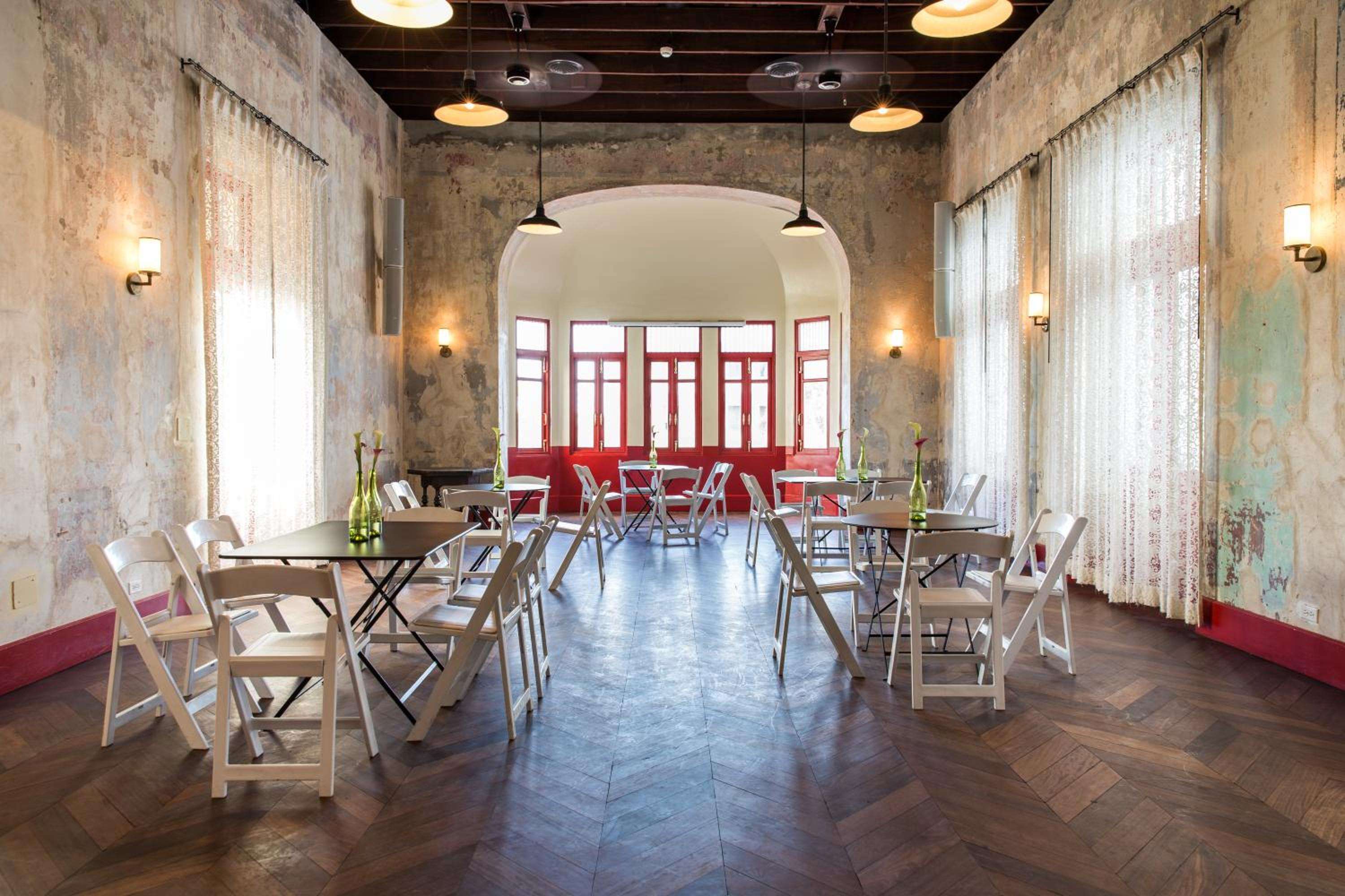 Weathered walls and vintage charm define this intimate meeting space, where folding chairs gather beneath pendant lights and red accents hint at Panama City's colonial heritage.