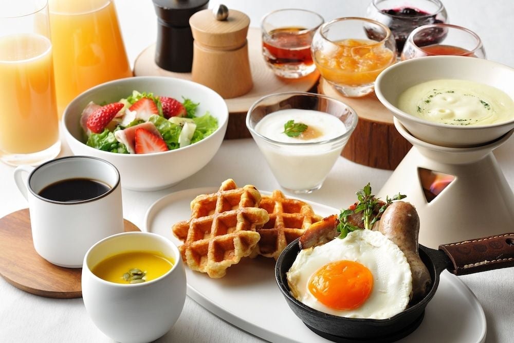 Morning light illuminates a thoughtfully curated breakfast spread where golden waffles meet perfectly fried eggs, fresh strawberries glisten alongside artisanal jams, and steaming coffee promises the perfect mountain morning ritual.