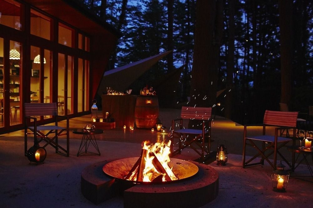 Crackling flames dance against the twilight as sparks drift skyward, while lanterns cast intimate pools of light across the modern mountain terrace.