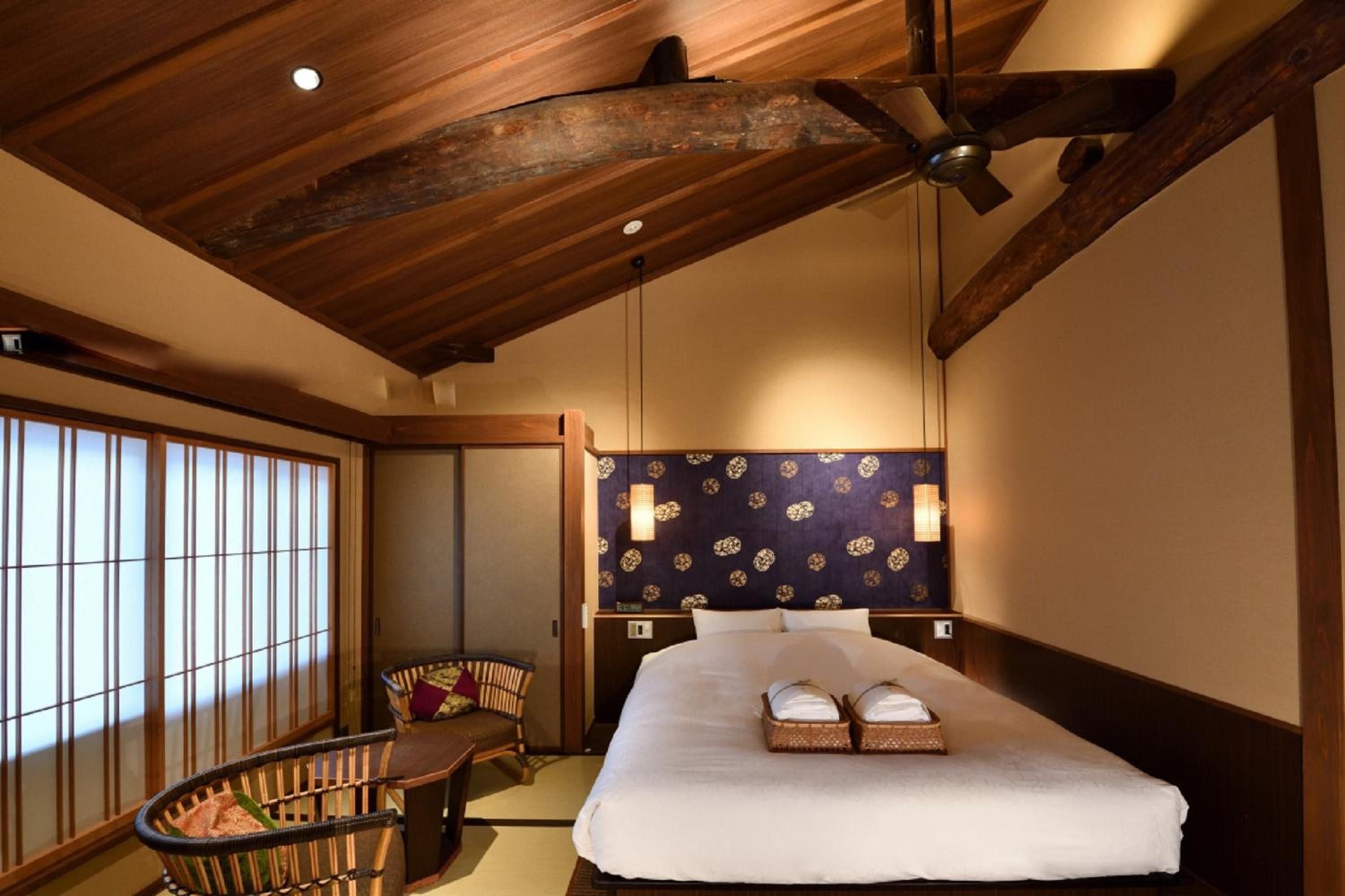 Exposed timber beams frame crisp white linens beneath a indigo accent wall, where traditional shoji screens filter Kyoto's gentle light into this serene sanctuary.