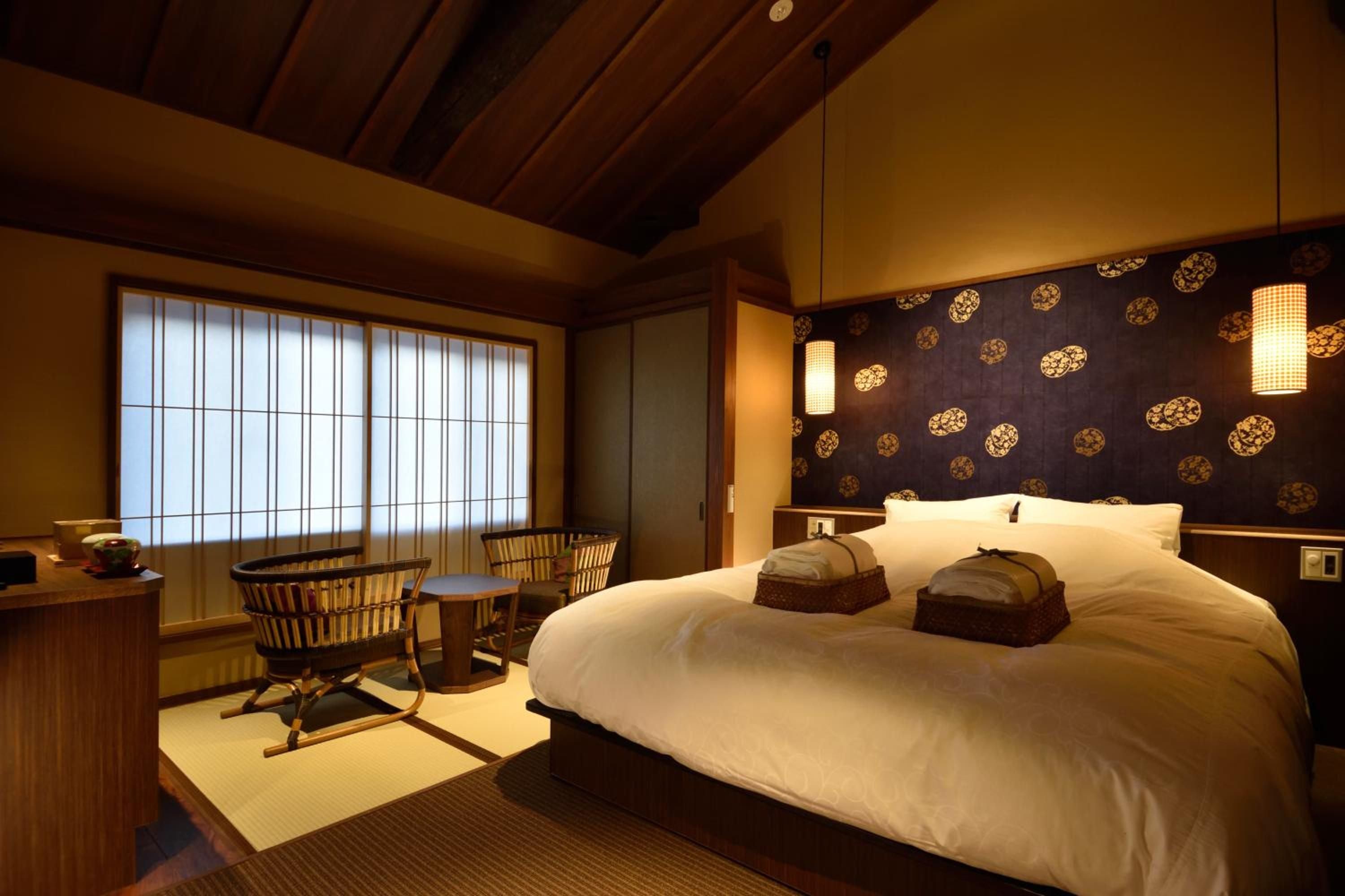 Exposed wooden beams frame this serene guest room where traditional shoji screens filter soft light across tatami mats and contemporary comfort meets timeless Japanese design.