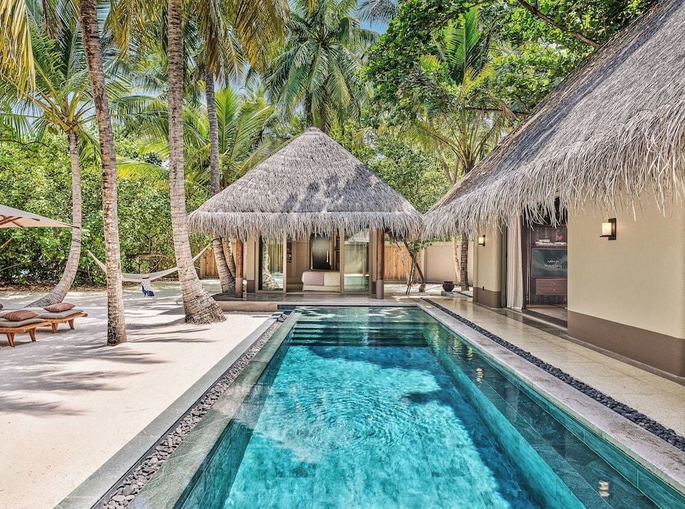 Crystal-clear waters reflect swaying palms beside this beach villa's private pool, where thatched roofs and warm timber create an intimate tropical sanctuary steps from pristine sand.