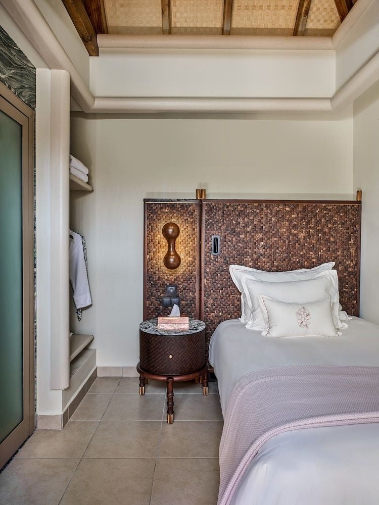 Handwoven rattan panels and copper accents create intimate warmth in this villa bedroom, where traditional Maldivian craftsmanship meets contemporary luxury beneath exposed timber beams.