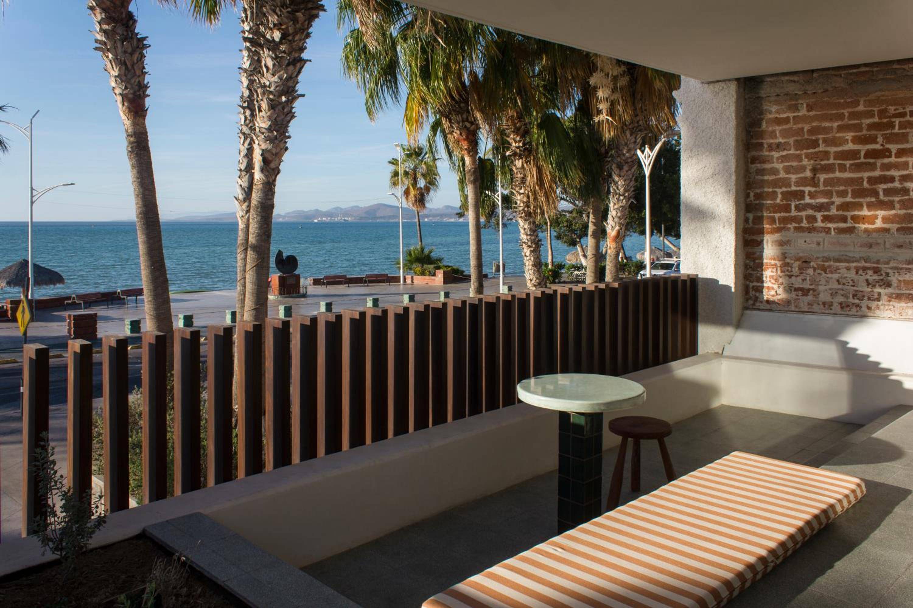 Weathered brick meets modern concrete on this sea-facing terrace, where vertical wood slats frame endless blue horizons and swaying palms of La Paz's waterfront.