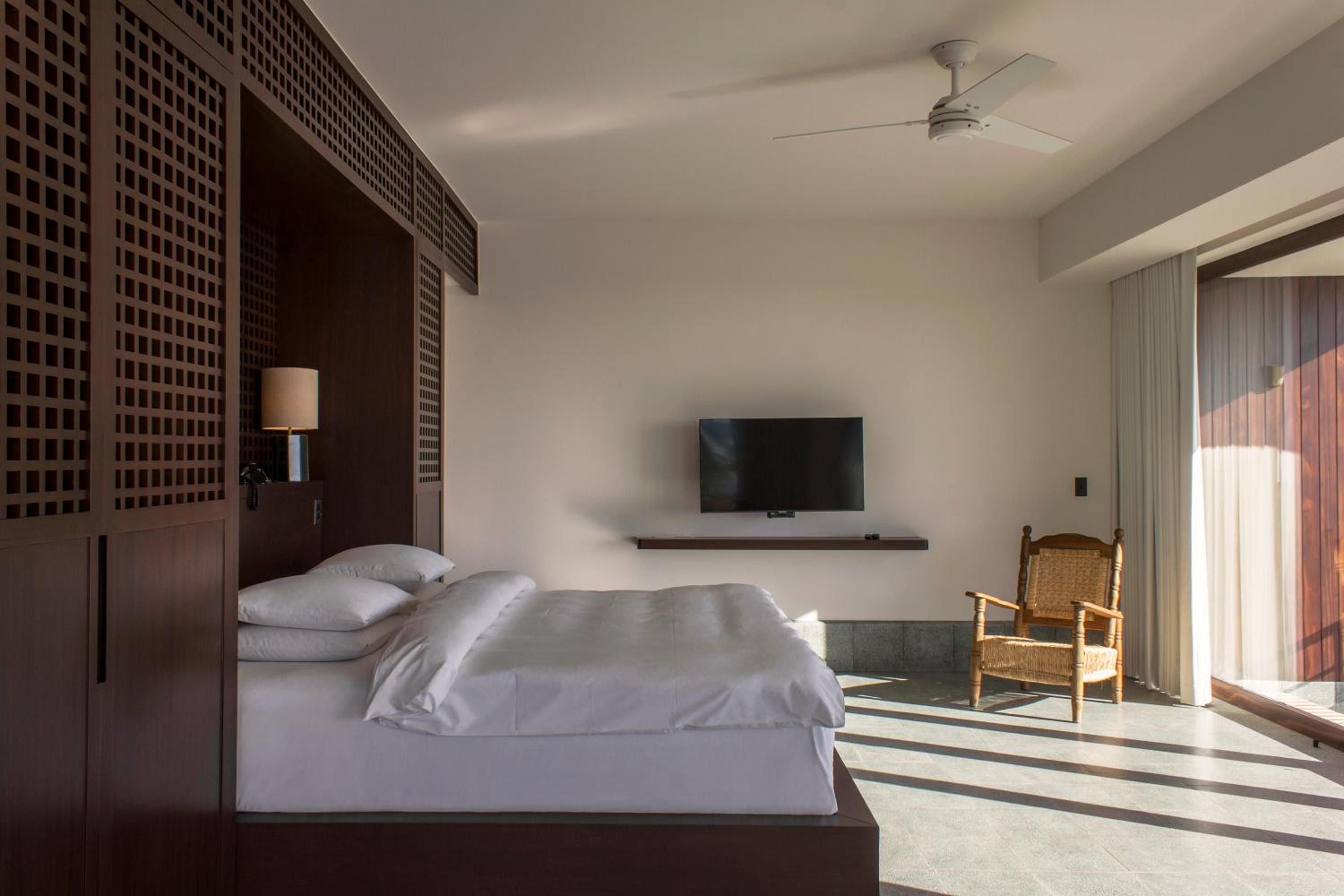 Geometric latticed screens frame the platform bed while woven textures and filtered sunlight create serene shadows across polished concrete floors in this minimalist sanctuary.