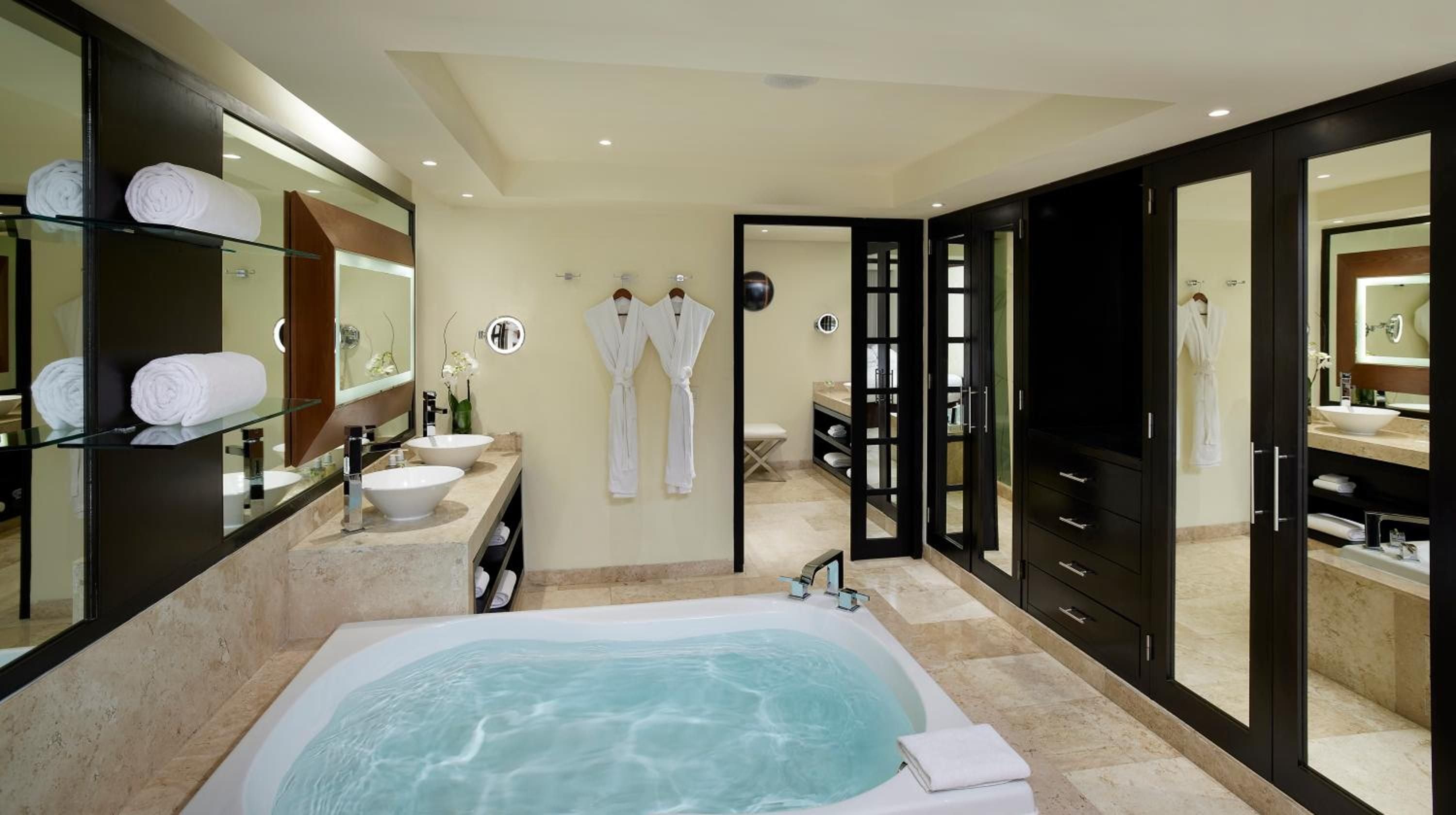 Marble surfaces and dark wood cabinetry frame a sunken soaking tub, while plush white robes await in this spa-like master bath sanctuary.