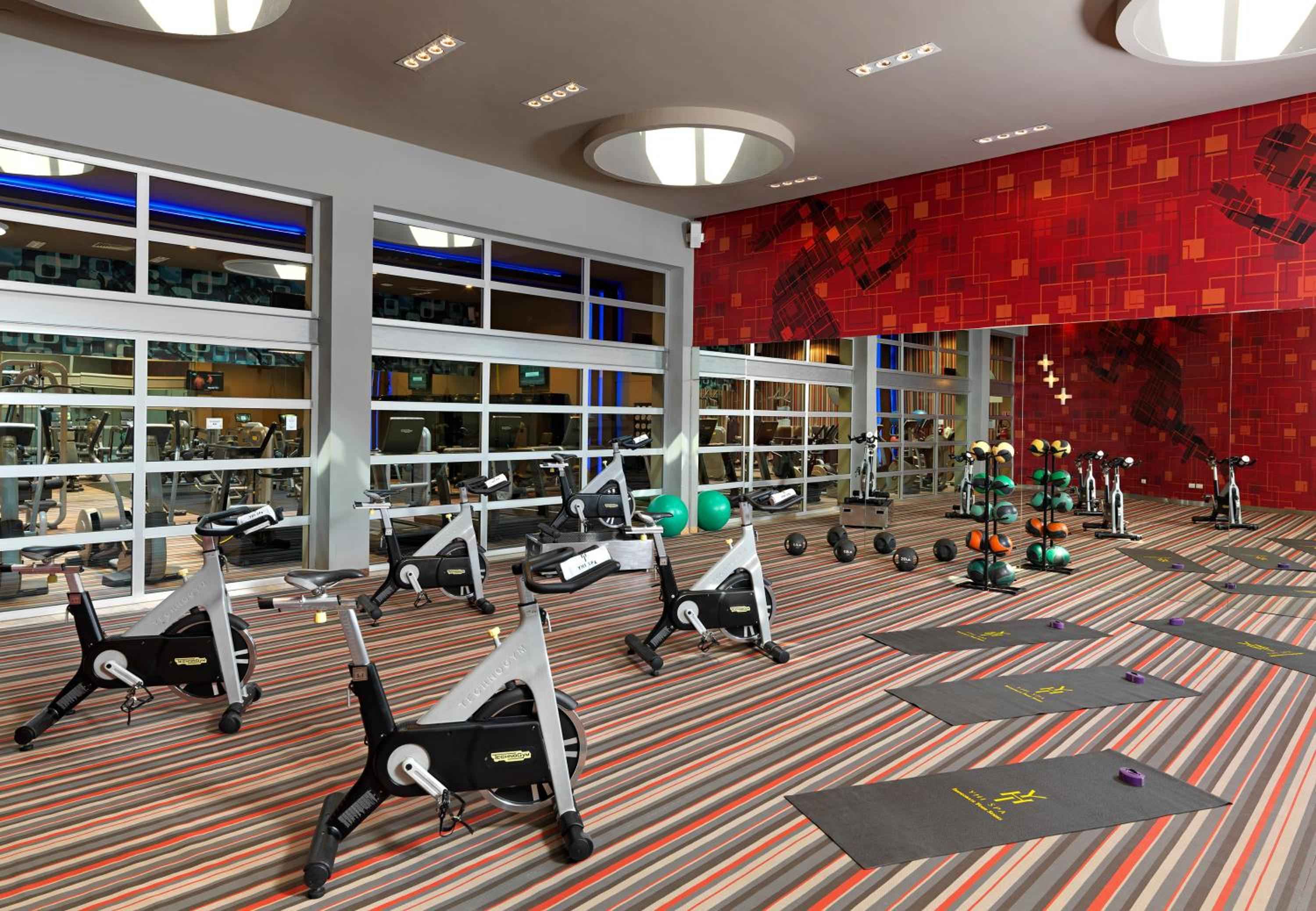Energizing spin classes await in this vibrant fitness studio where red mosaic walls create dynamic patterns and floor-to-ceiling windows flood the space with natural light.