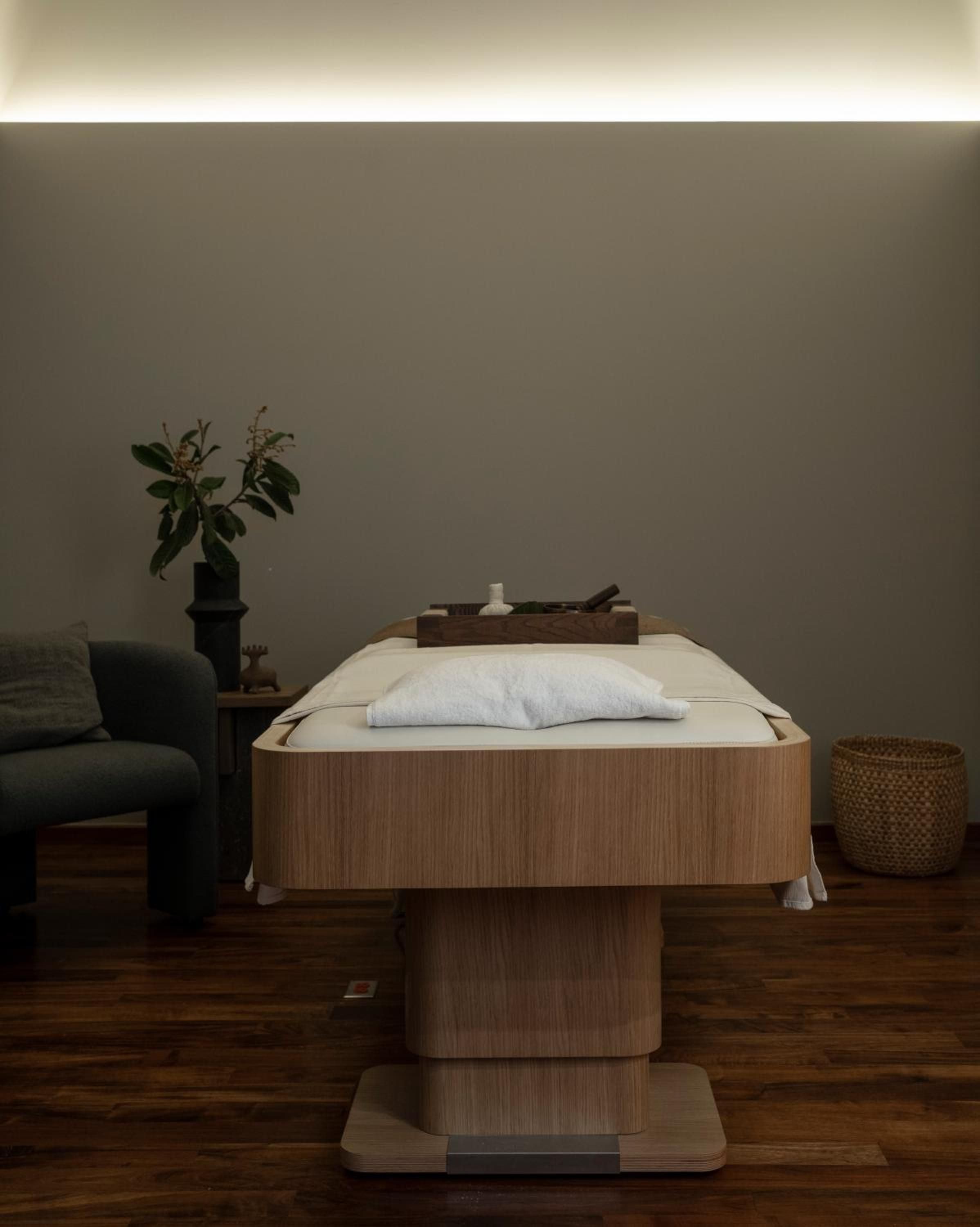 Warm wood tones and soft lighting create an intimate sanctuary where minimalist design meets thoughtful wellness rituals in this serene treatment room.