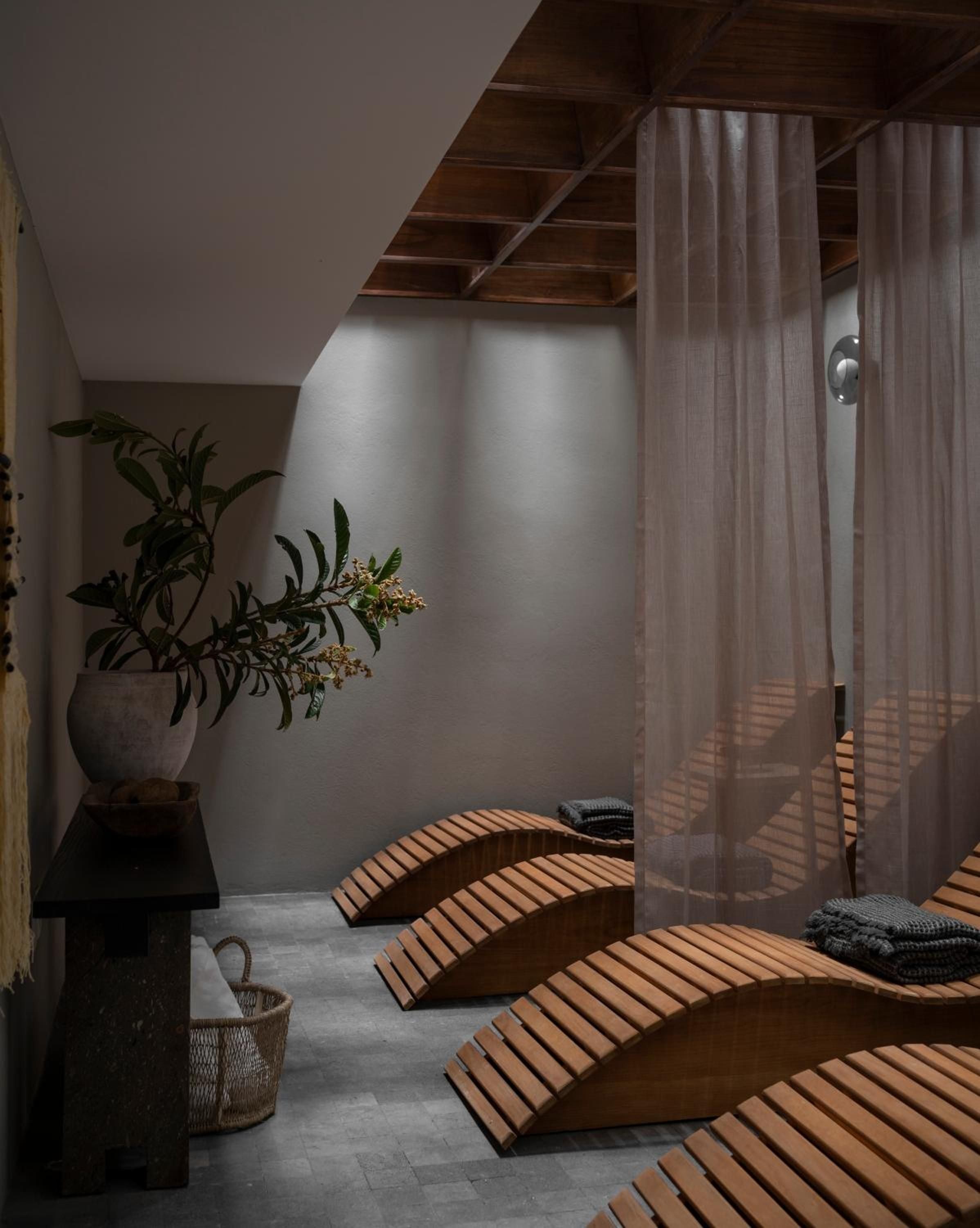 Curved wooden loungers beckon beneath exposed beams while sheer curtains filter golden light across this serene spa sanctuary, creating an intimate retreat for restoration.