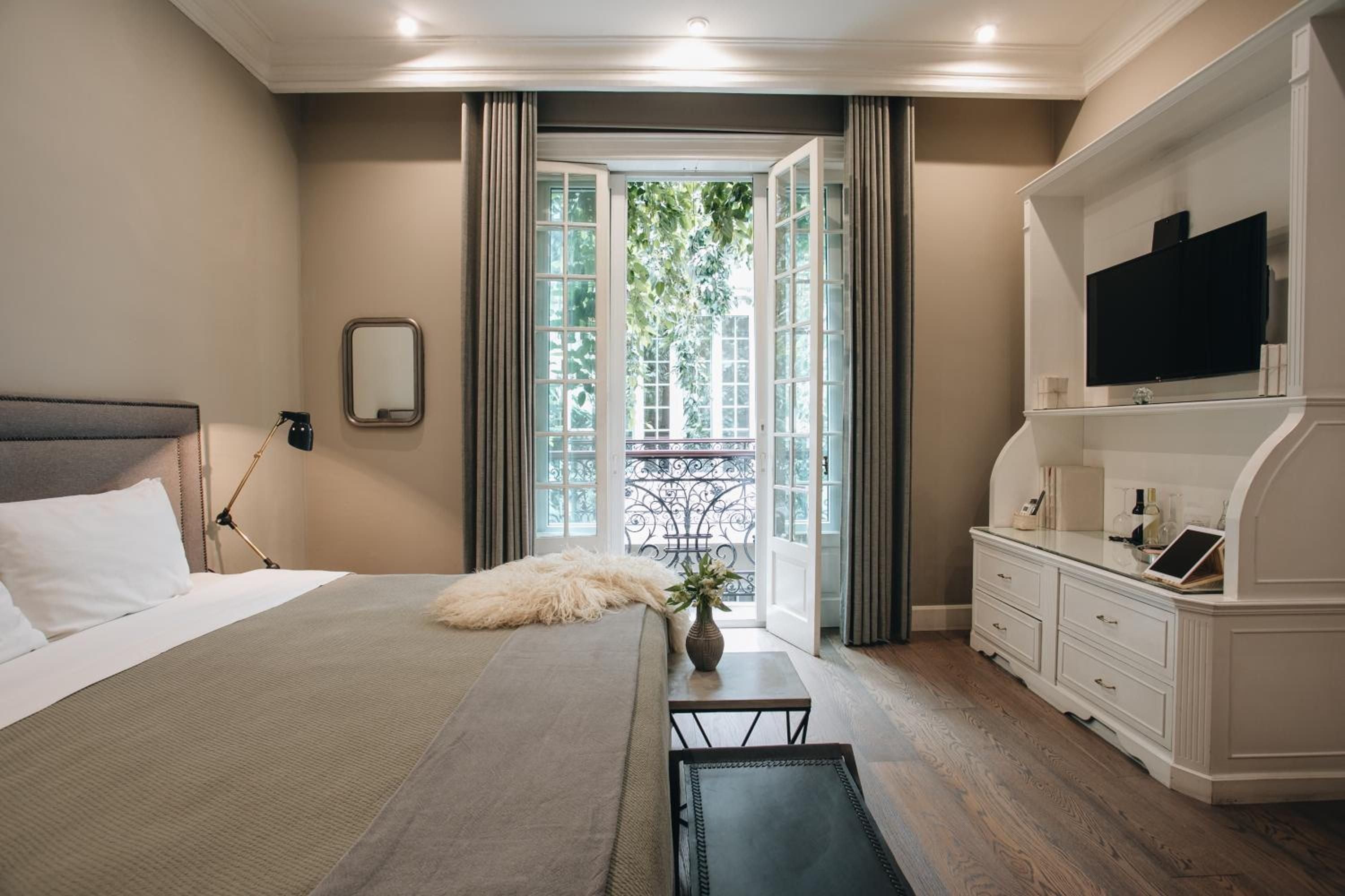 Neutral tones and crisp linens create a serene retreat, while French doors open to a wrought-iron balcony framed by leafy views.
