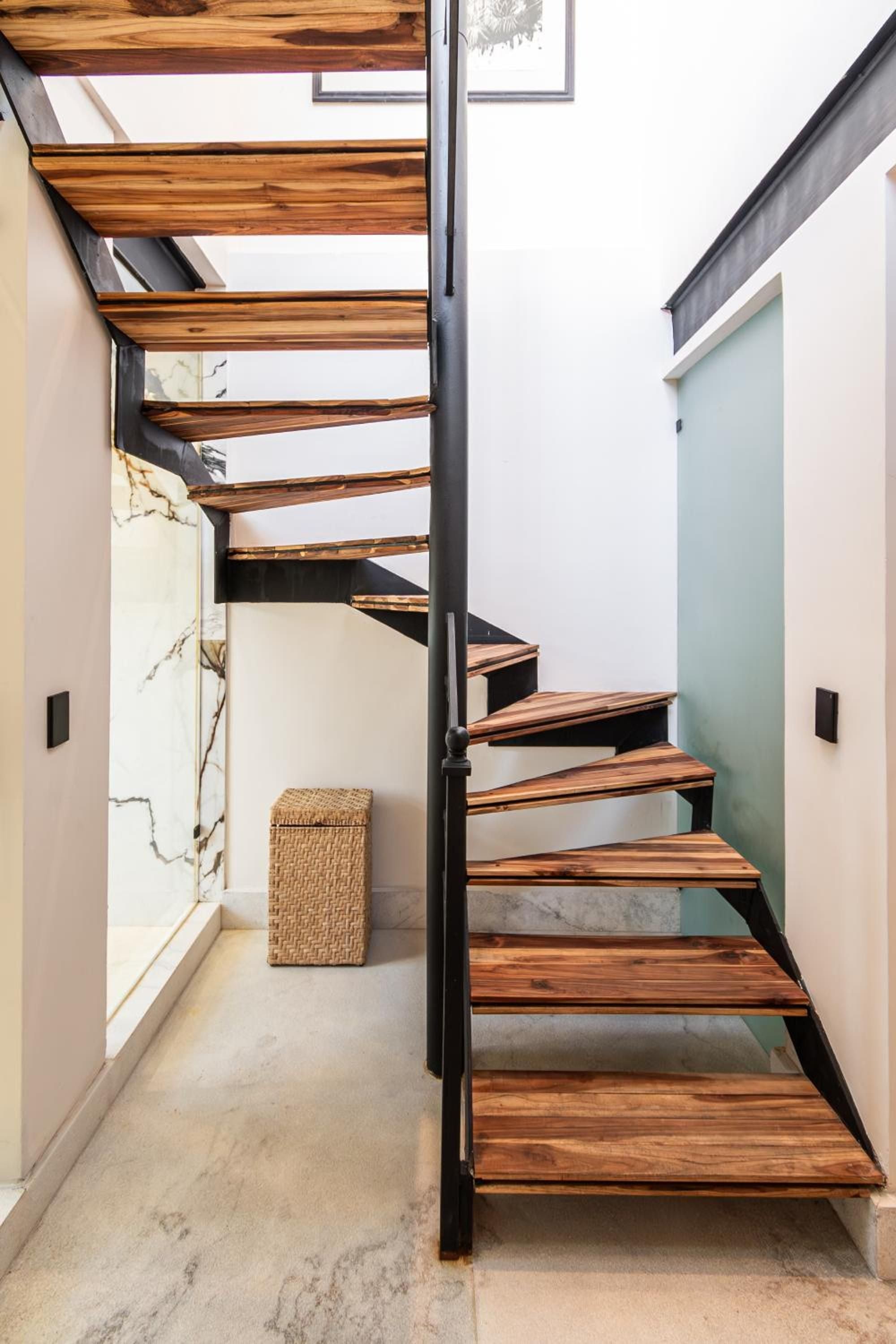 Floating timber treads and blackened steel railings create an sculptural staircase, where warm wood grains contrast beautifully against crisp white walls and polished concrete floors.