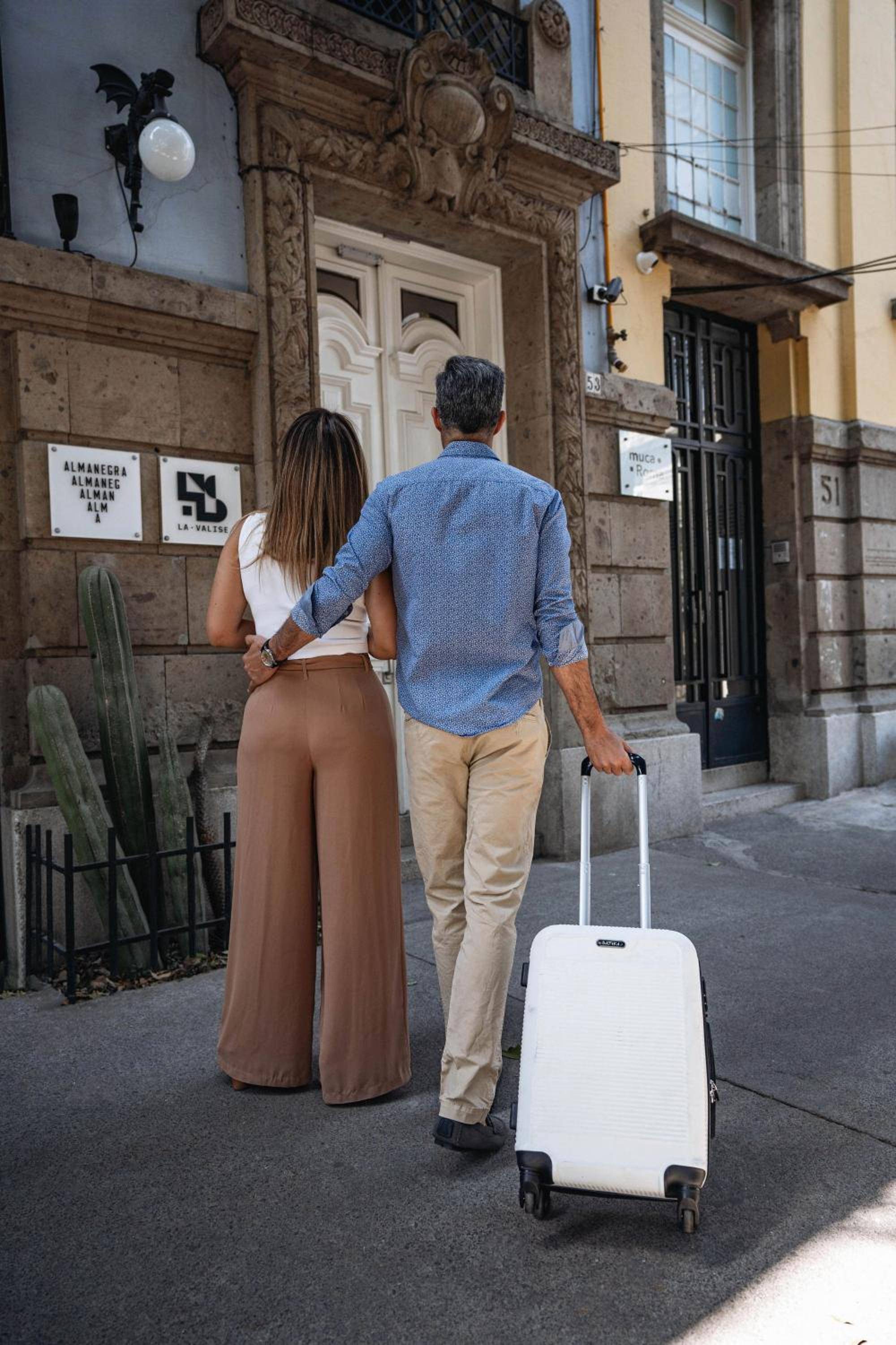 Colonial stone archways and ornate carvings frame the hotel entrance as guests arrive with luggage, wheeling through centuries of Mexican architectural heritage.