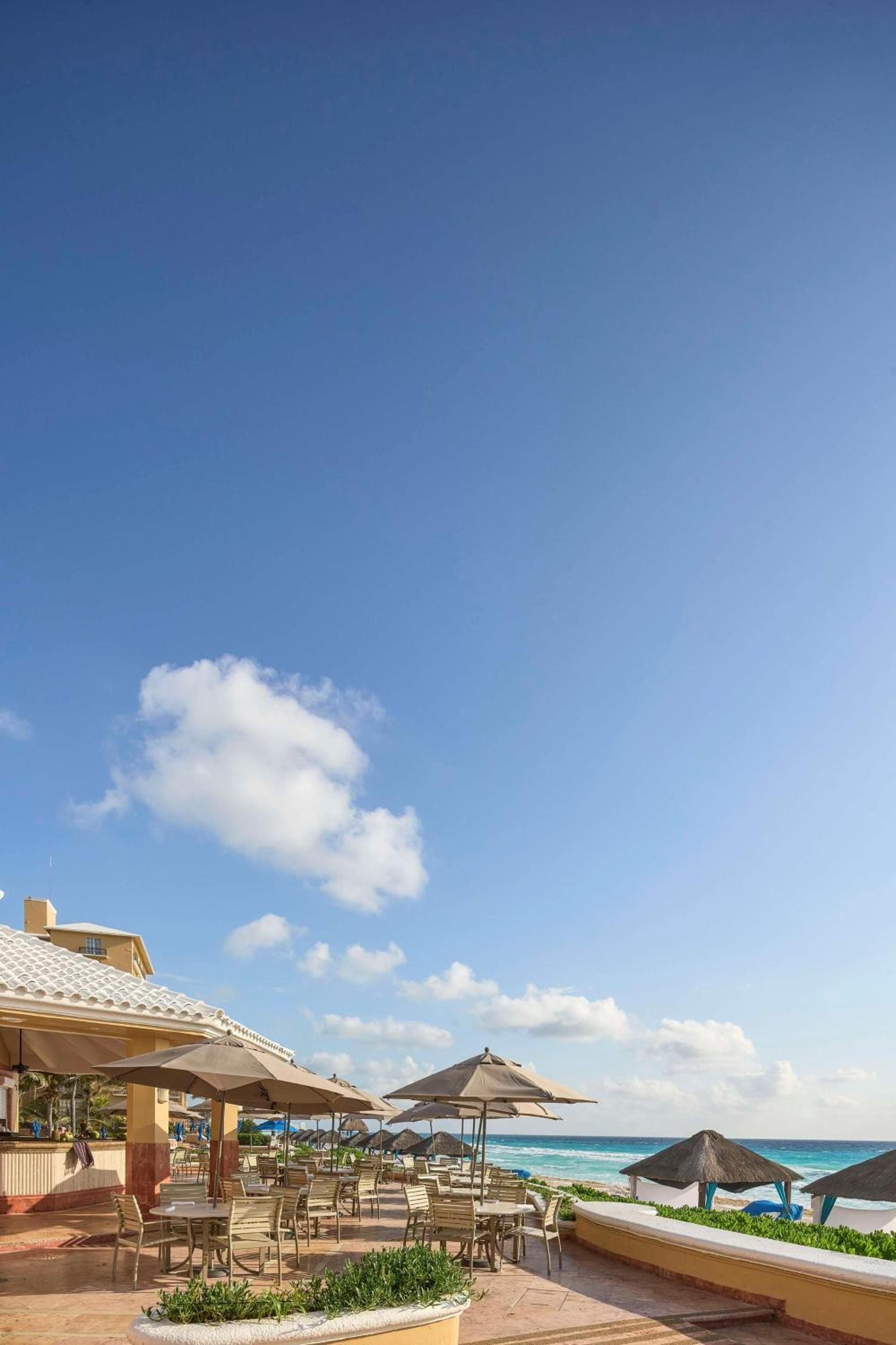 Oceanfront dining unfolds under neutral umbrellas where turquoise Caribbean waters meet golden sand, creating an idyllic backdrop for leisurely meals steps from the shore.