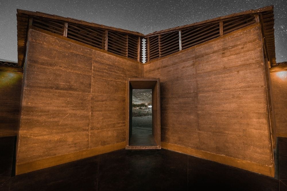 Raw earth walls embrace a minimalist doorway beneath star-scattered desert skies, where contemporary Mexican architecture meets ancient adobe traditions in perfect harmony.