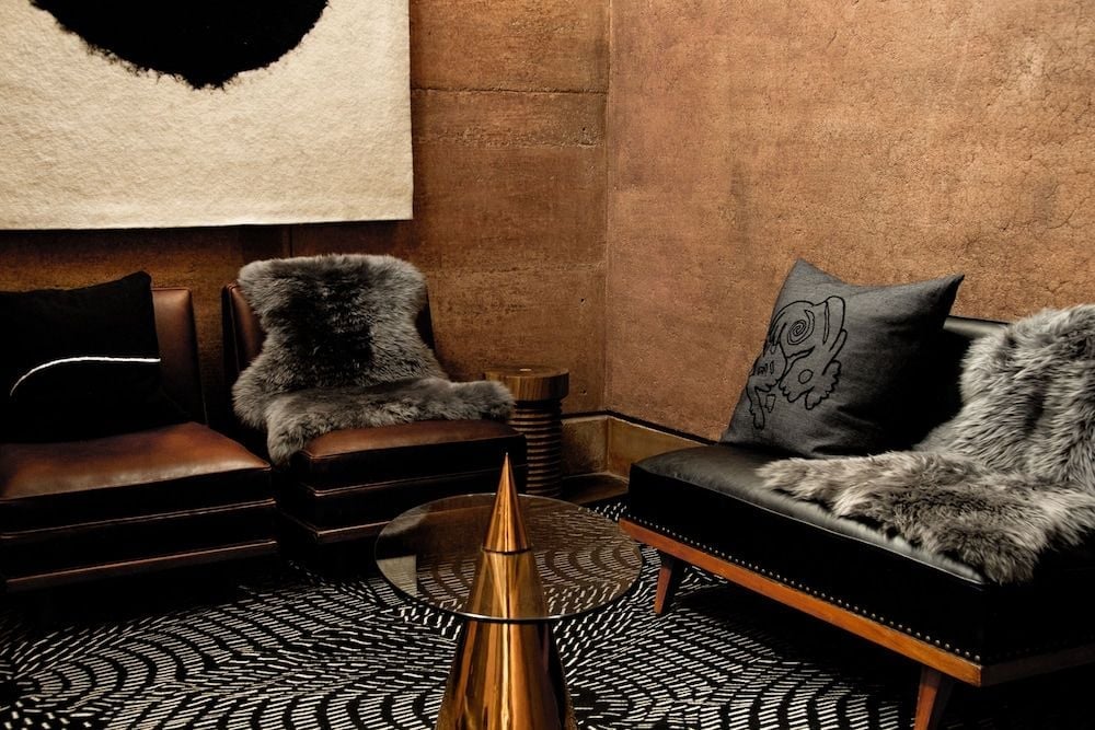 Luxurious leather seating and plush fur throws create an intimate lounge where golden cone sculptures catch warm light against textured adobe walls.