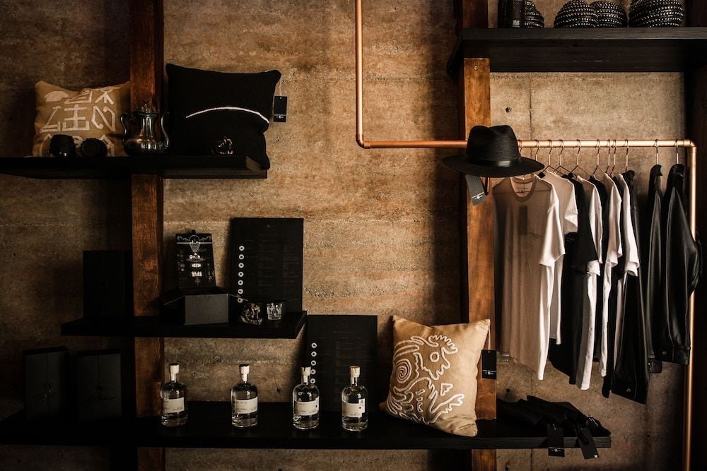 Industrial-chic shelving displays artisanal spirits and curated clothing in warm lamplight, where raw concrete meets copper piping in this sophisticated guest suite.
