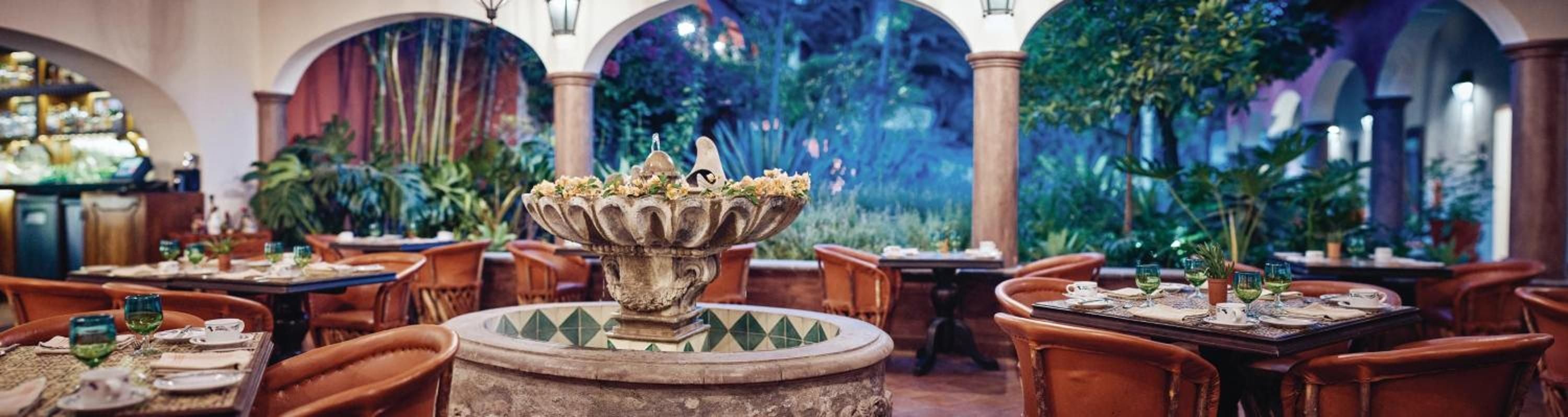 Arched stone colonnades frame intimate dining tables around a decorative fountain, while vibrant murals transport guests to an enchanted underwater world.