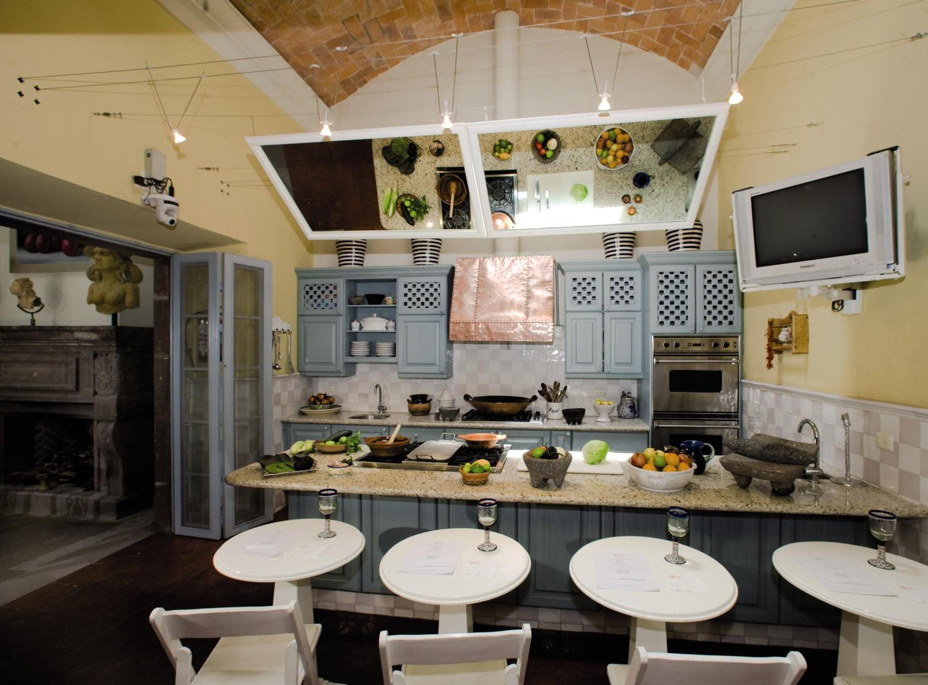 Copper gleams against sage-green cabinetry in this culinary demonstration kitchen, where brick vaulting frames an artful display of Mexican cooking traditions and fresh ingredients.