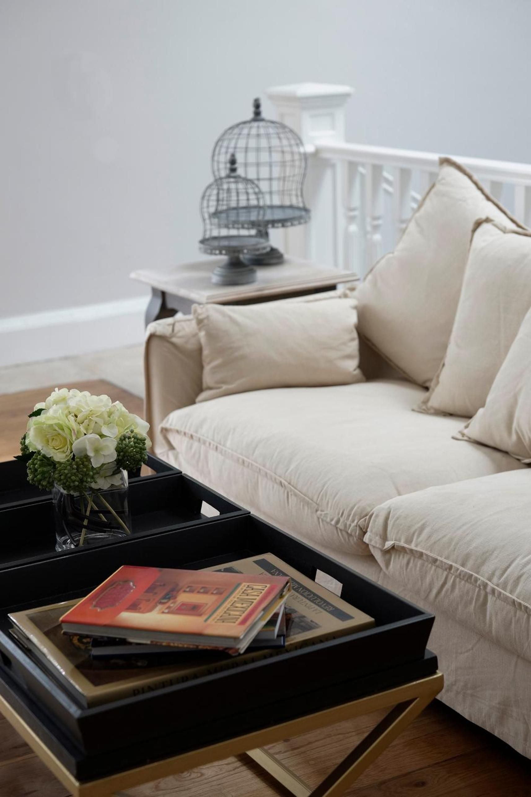 Cream linen cushions and weathered birdcages create an effortlessly elegant sitting area where afternoon light filters through, inviting quiet contemplation with coffee table books.