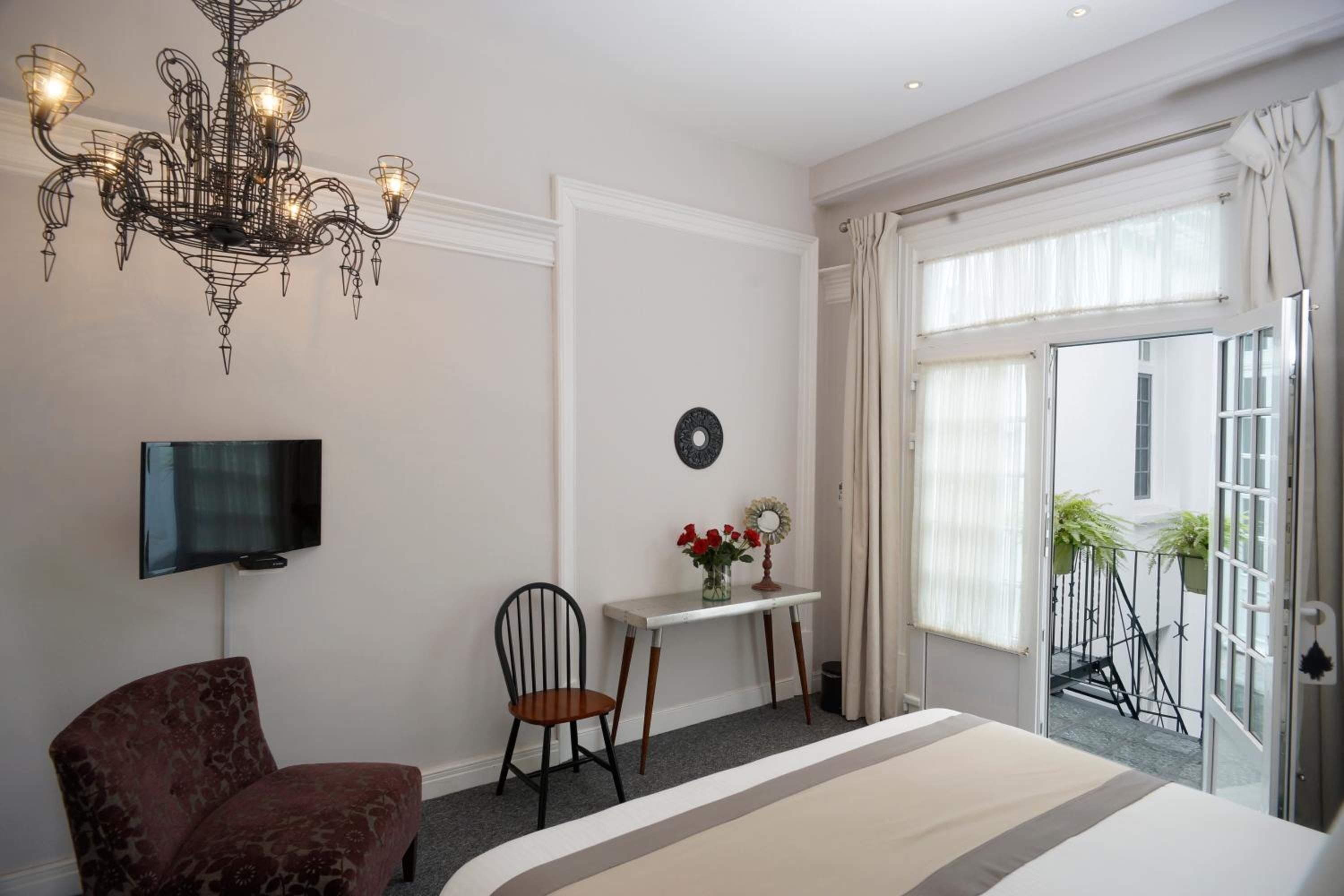 Ornate wrought-iron chandeliers cast warm light across crisp linens while French doors open to a private balcony overlooking the charming courtyard below.