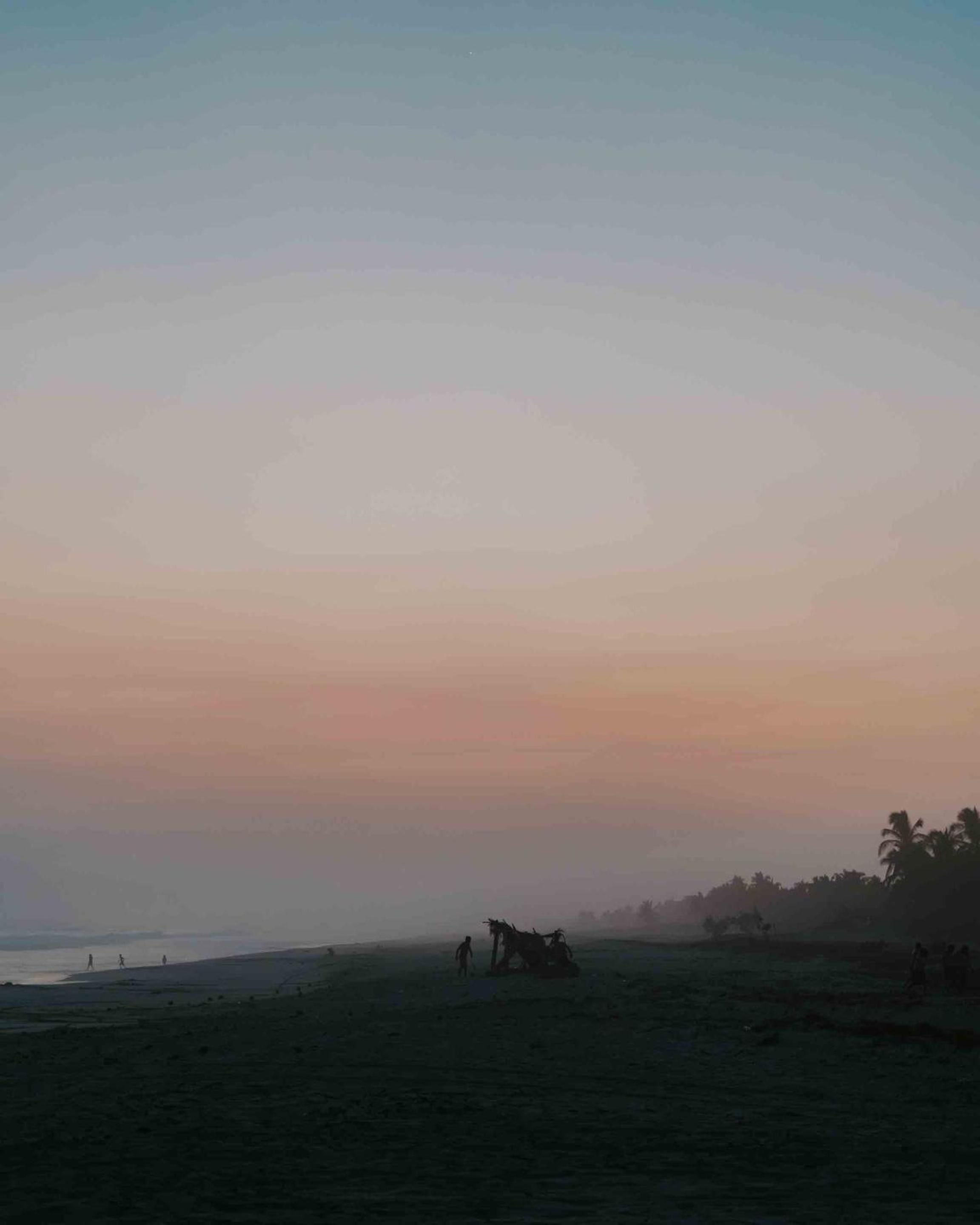Sunset paints Puerto Escondido's coastline in soft pastels as silhouettes gather on the sand, creating an intimate evening tableau beyond Casa Yuma's oceanfront setting.
